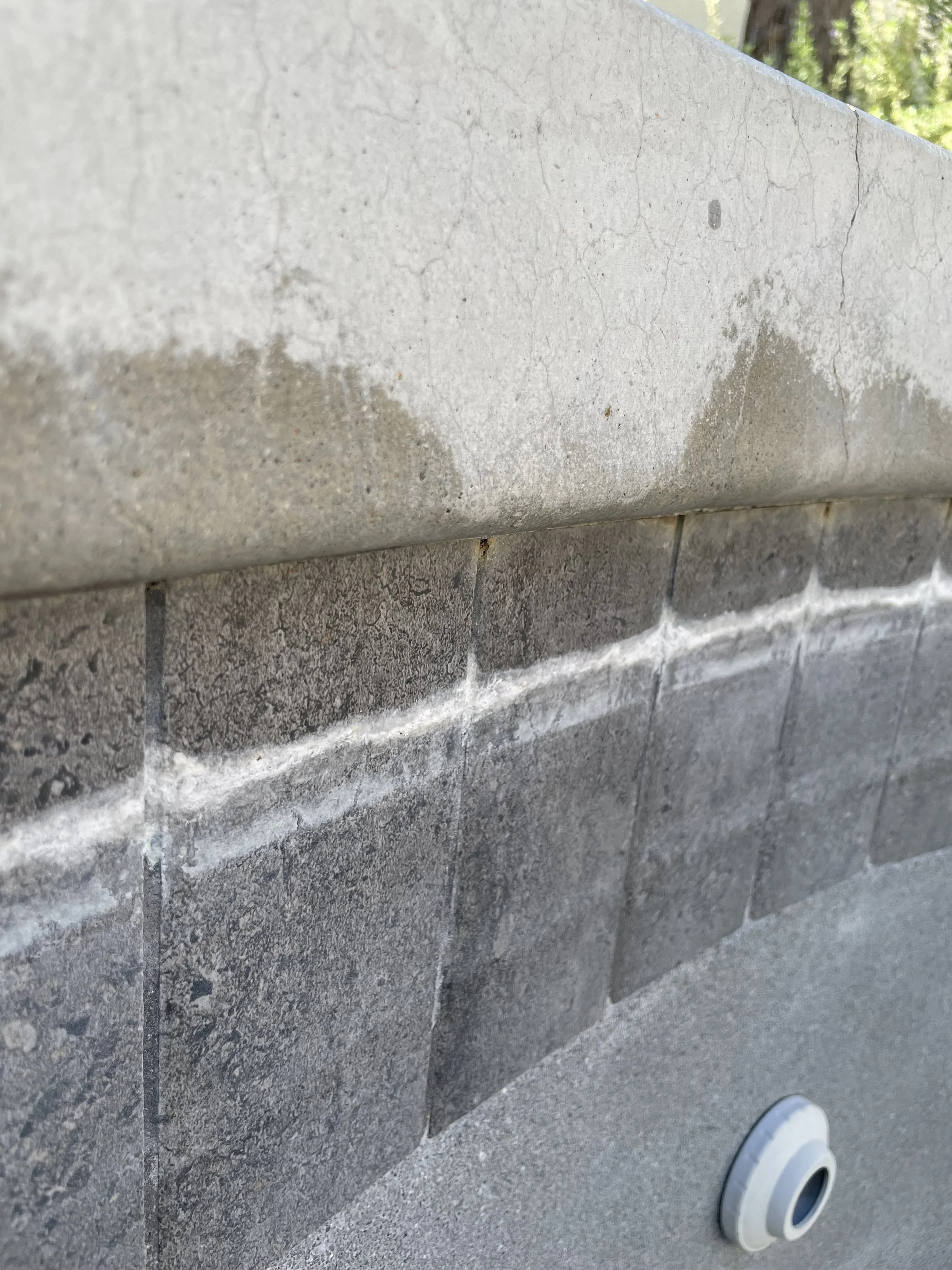 Close-up of a concrete wall with a white line of caulking and a metal pipe fitting at the bottom right.