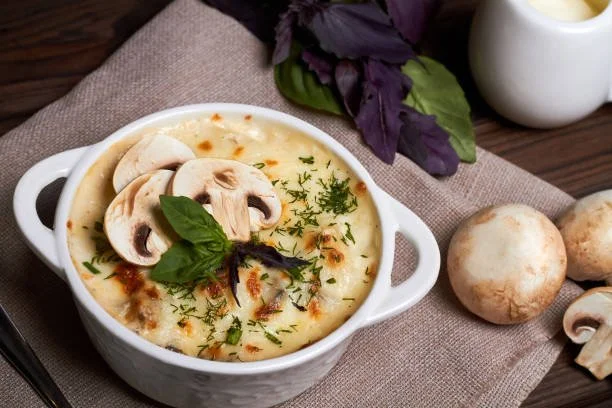 Creamy mushroom soup garnished with fresh herbs and sliced mushrooms on top, with whole mushrooms and basil leaves nearby.