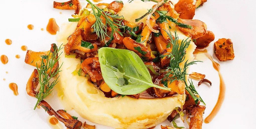 A white bowl with mixed salads, diced raw fish, rice, avocado, and dressing on a round wooden plate with a white cloth underneath on a green background.