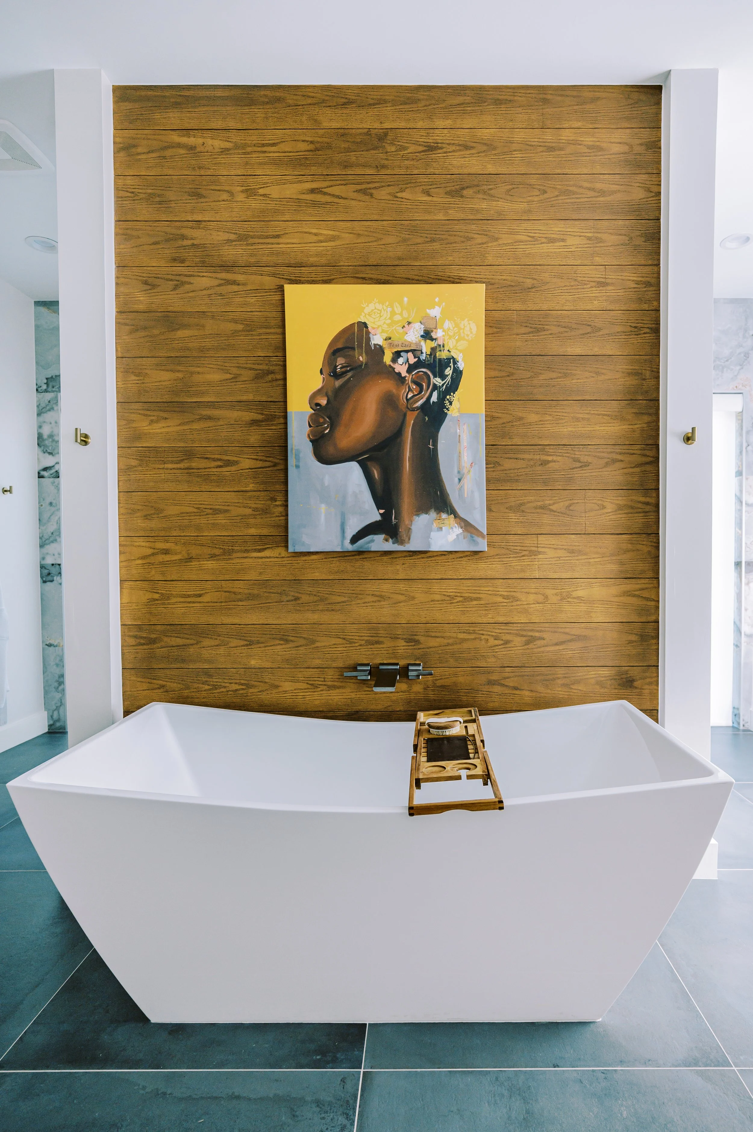 High-end custom bathroom with freestanding soaking tub, wood accent wall, and curated artwork.