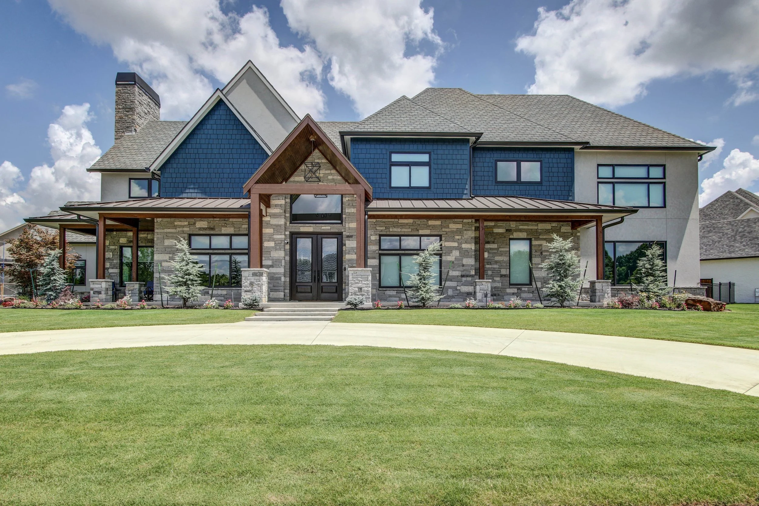Luxury custom home exterior with stone façade, timber entry detail, blue siding, and modern mountain architecture.
