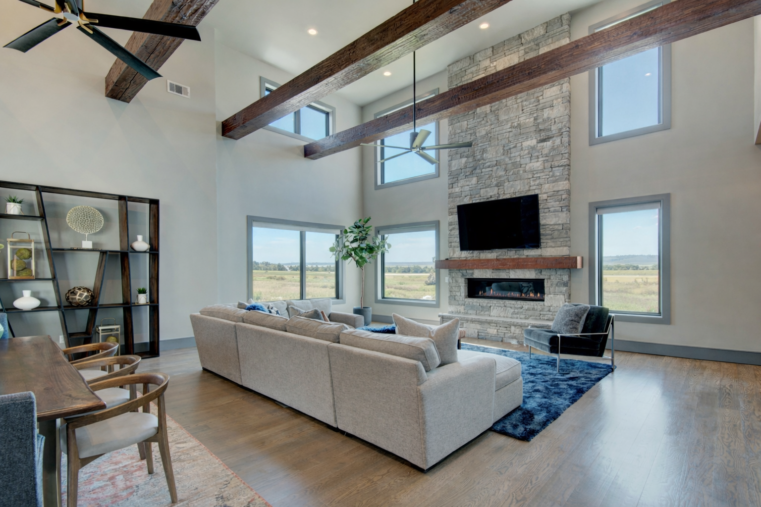 Open-concept mountain modern great room featuring exposed wood beams, stone fireplace, and expansive views.