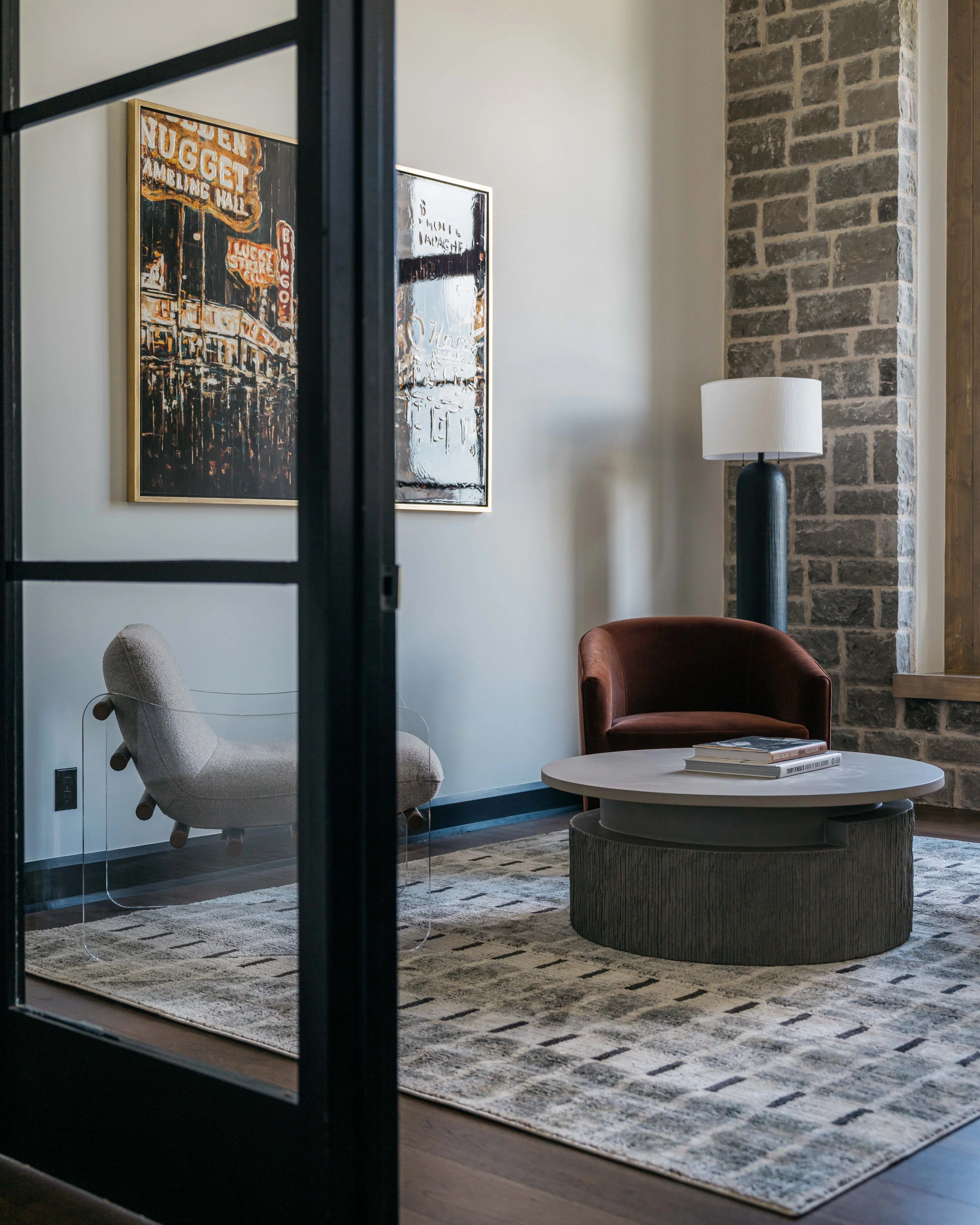Modern commercial office lounge with glass partition, custom furnishings, brick accent wall, and refined interior finishes.