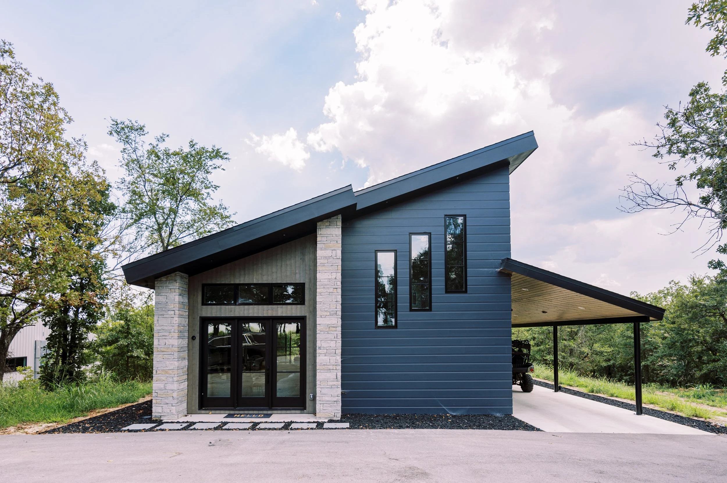 Modern luxury custom guest house with sloped roofline, stone accents, dark siding, and covered carport.