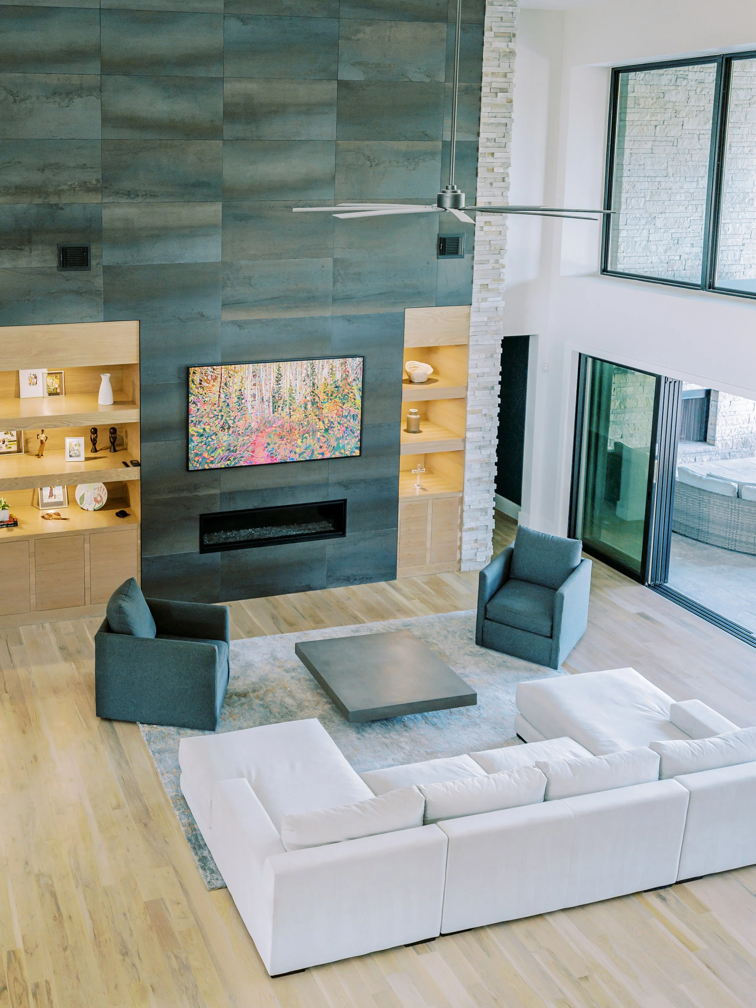Luxury custom home living room with double-height ceiling, stone feature wall, modern fireplace, and custom built-ins.