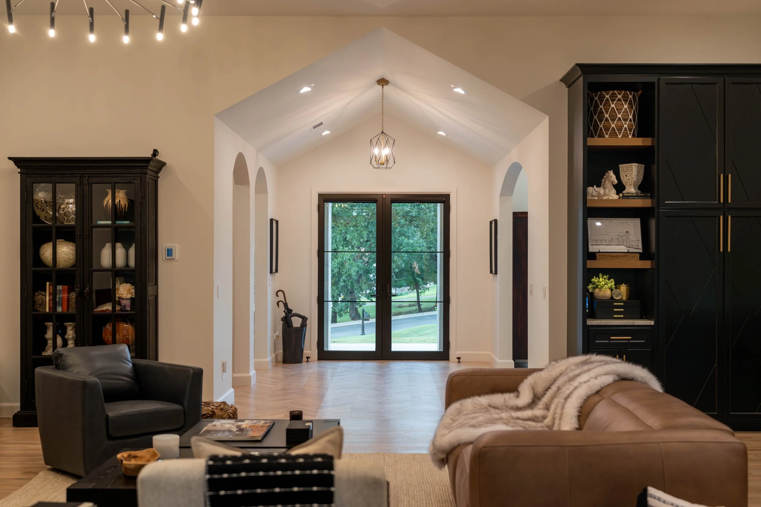 Luxury custom home entryway with vaulted ceiling, arched hallways, wood flooring, and large glass doors opening to the landscape.