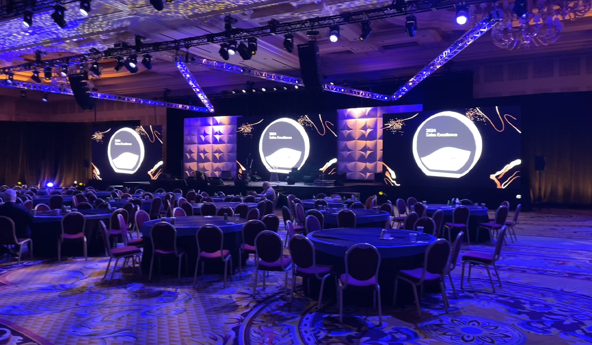 Conference hall with round tables and chairs facing a large stage with three screens displaying 'Skills Excellence 2024' at a formal event.