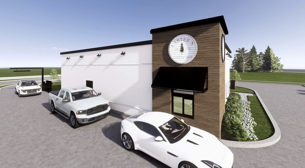 Exterior view of a modern restaurant building with a wooden facade and a round sign that says 'Ritter's' with a tree logo. There are three white cars parked outside on a paved lot, with a small landscaped area with bushes and grass nearby. The sky is clear.