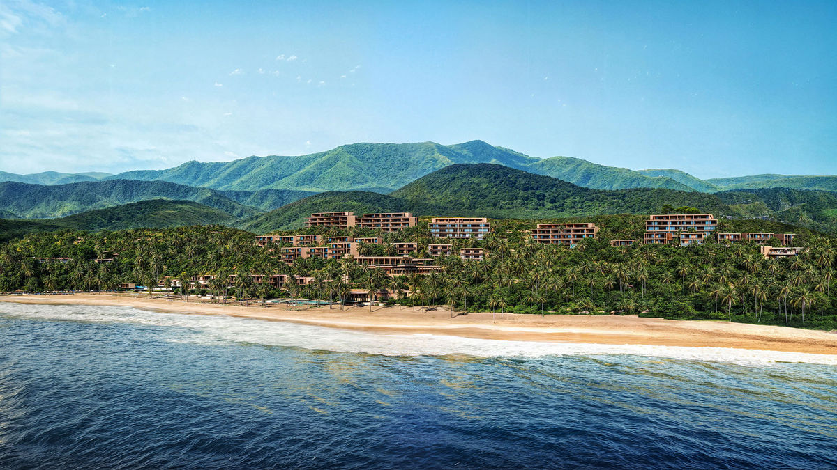 Tropical beach with palm trees, beachfront buildings, green hills, and mountains in the background under a blue sky.