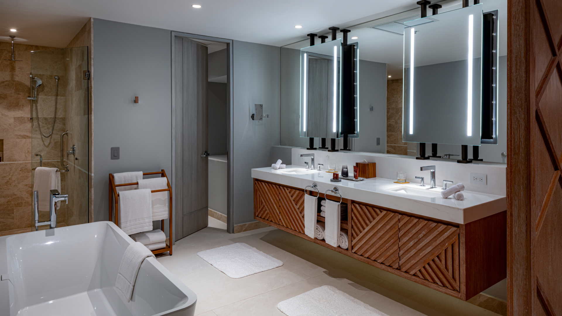 Modern bathroom with double vanity, large mirrors, illuminated mirrors, towels, and a bathtub, with a shower area in the background.