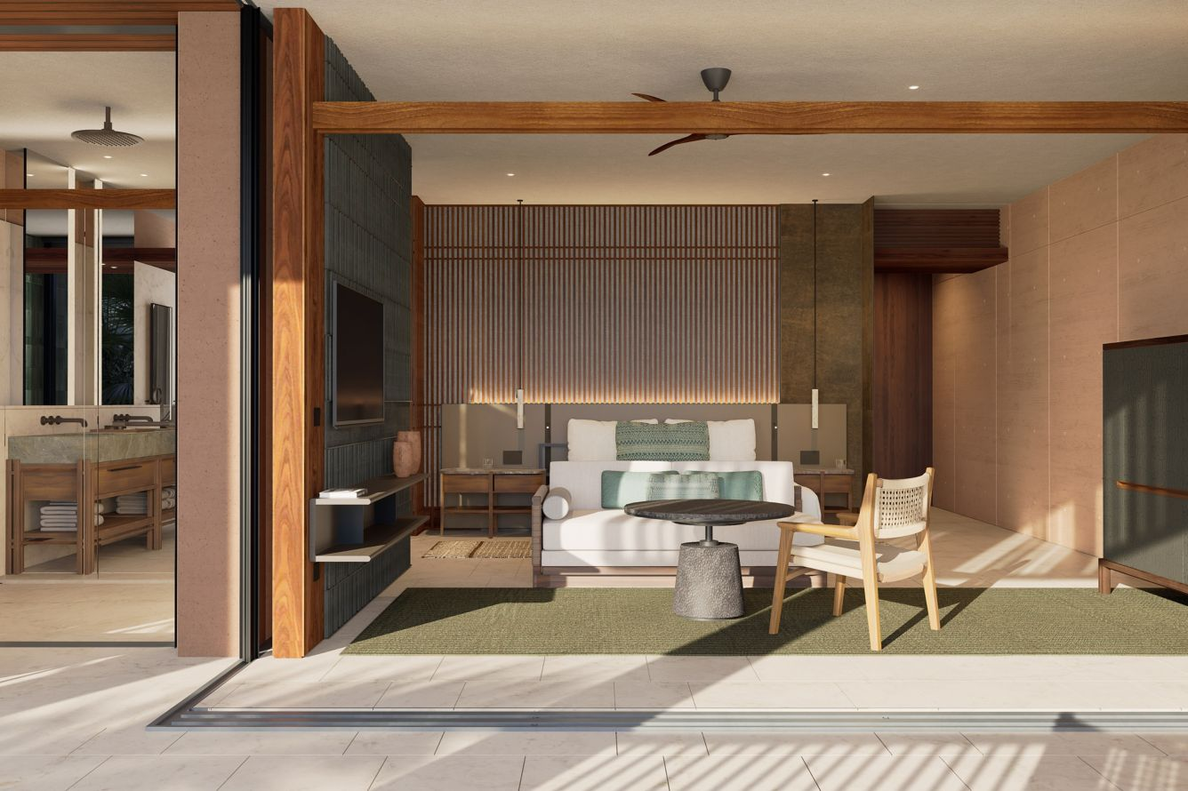 Interior view of a modern living room with a white sofa, a round black table, a wooden chair, and a TV mounted on a textured wall. Large sliding glass doors open to an outdoor area.