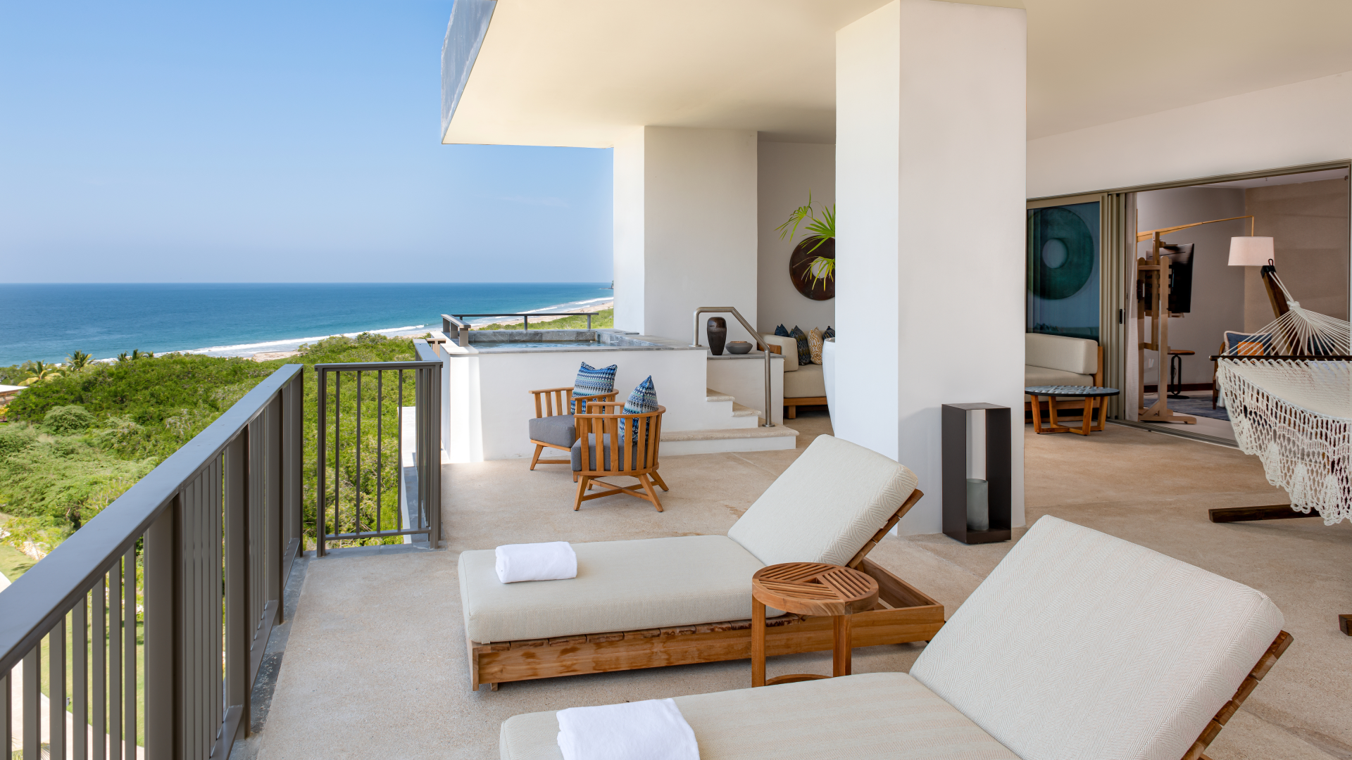 Balcony with two lounge chairs and a view of the ocean and green landscape, part of a modern coastal hotel suite with outdoor seating