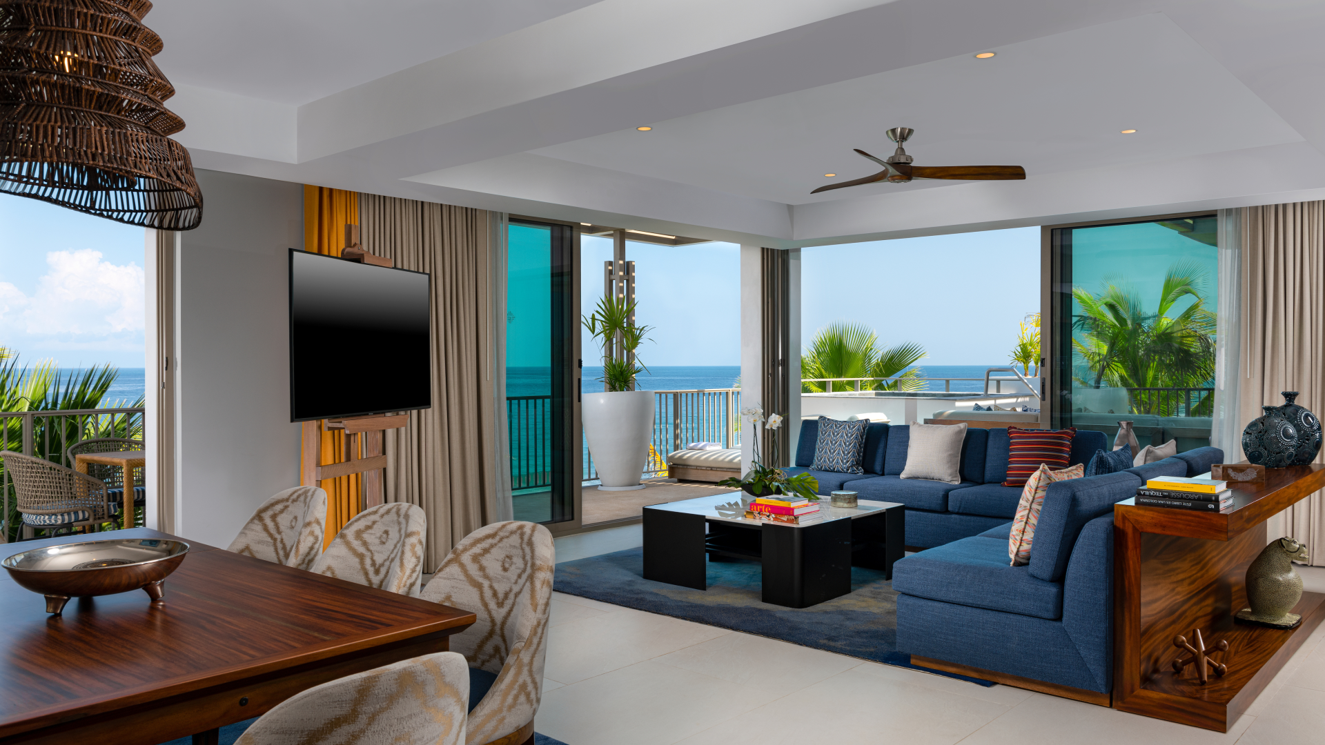 Living room with large windows, ocean view, blue sectional sofa, coffee table, potted plants, and balcony.