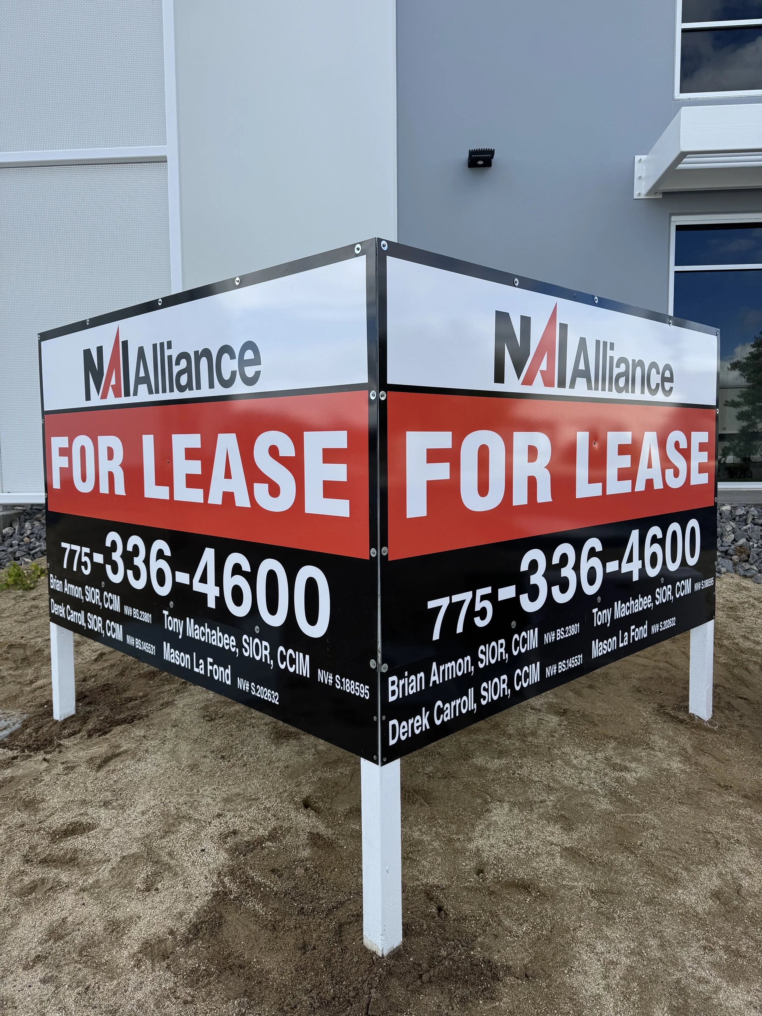 A sign on a lawn advertising property for lease by NA Alliance, displaying contact number 775-336-4600 and names Brian Armon, Tony Machabee, and Derek Carroll.