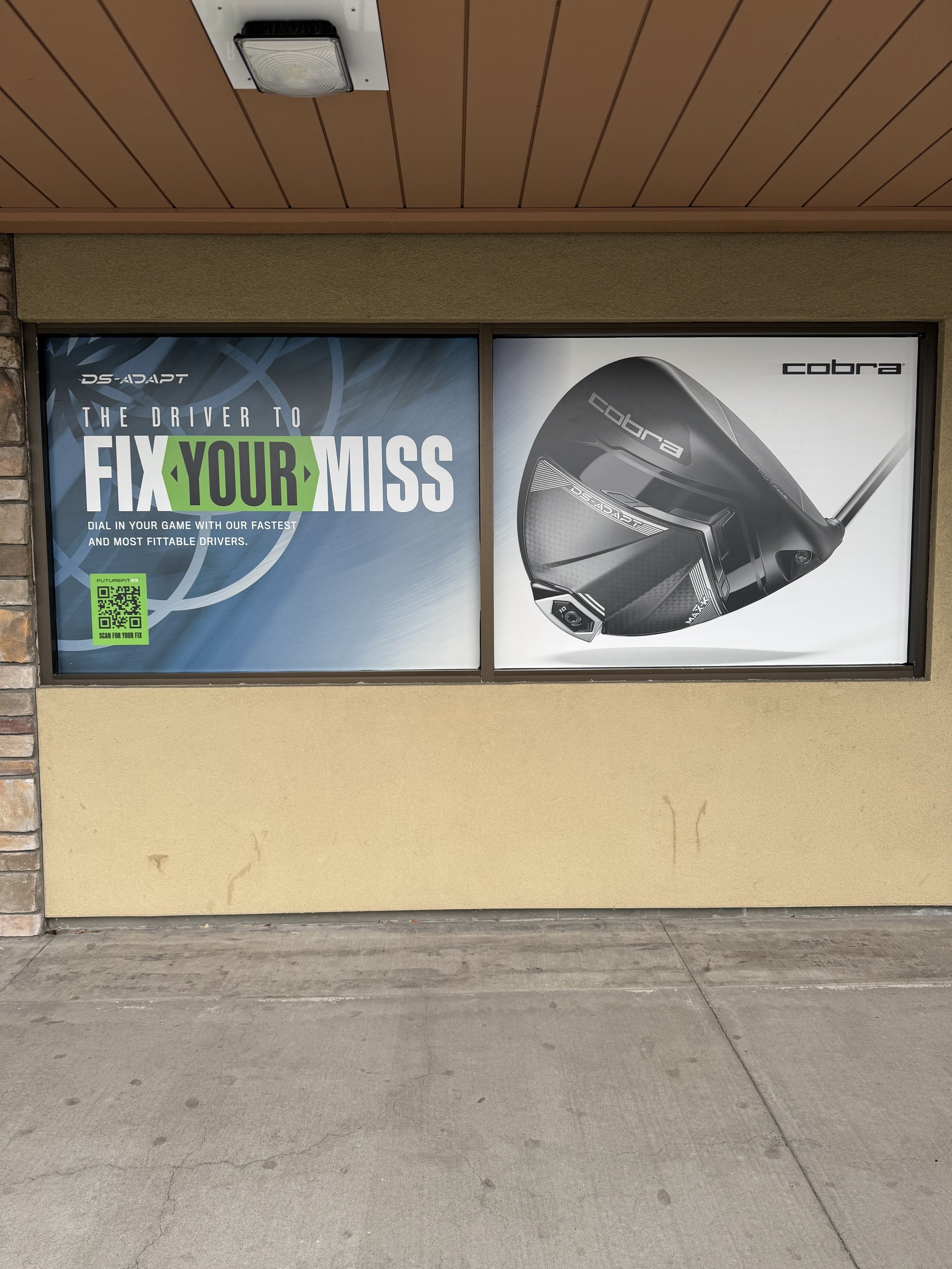 Advertisement for Cobra golf clubs featuring a large golf driver and text about fixing your golf swing on a window.