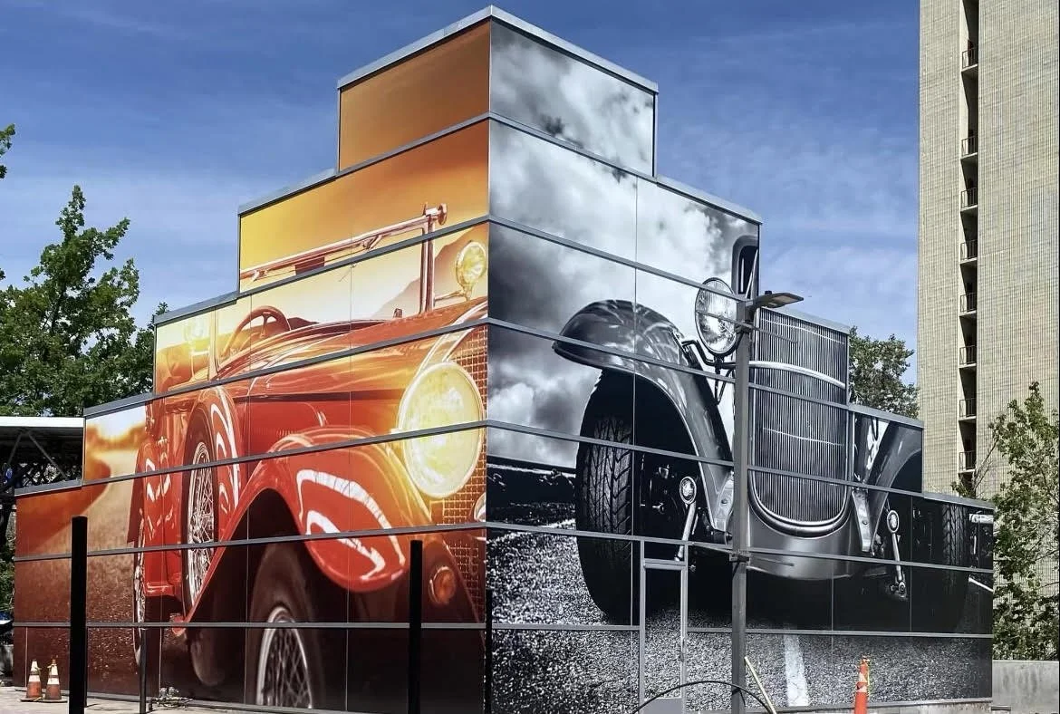 Large mural on a building depicting two vintage cars, one red with a sunny background and one black with stormy clouds, separated vertically.