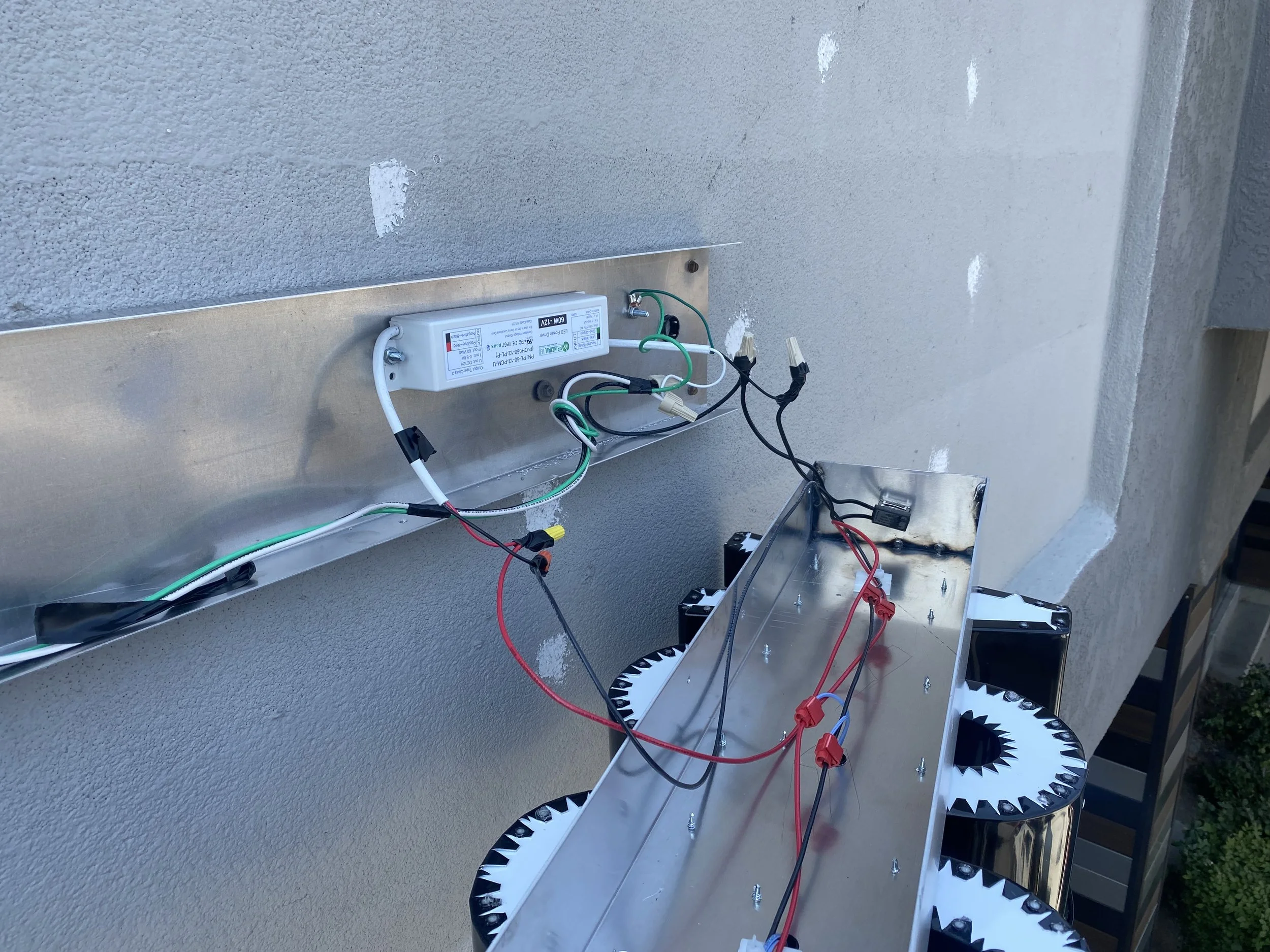 Close-up of an LED lit sign installation, with exposed wires and electronic components, and a metal frame structure.