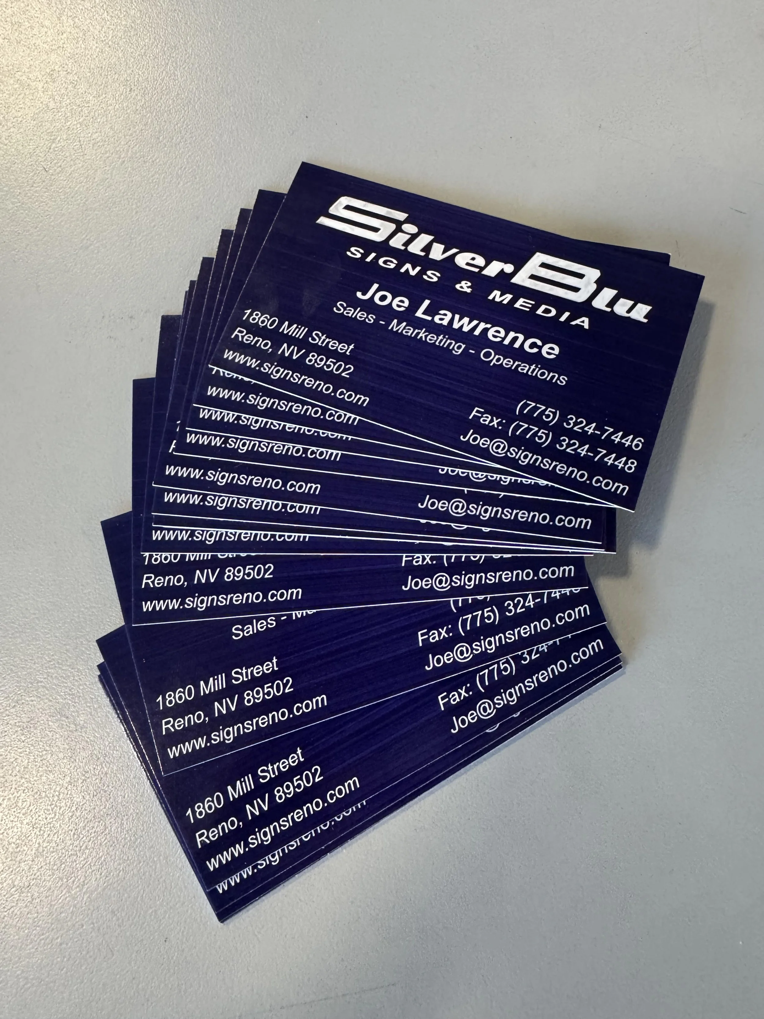 A stack of business cards for SilverBlu Signs & Media featuring Joe Lawrence with contact details, business address in Reno, Nevada, and website information.