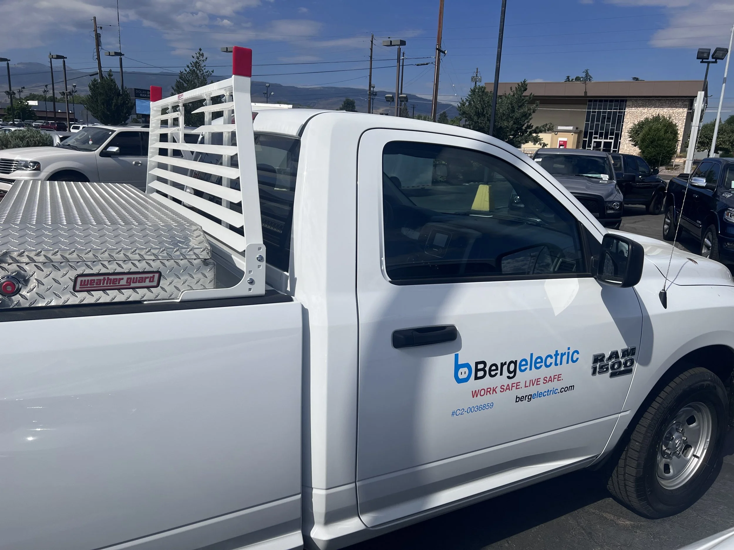 White pickup truck with Bergelectric logo and safety slogans parked in a lot, carrying a weather guard metal toolbox and a large metal storage box in the bed.