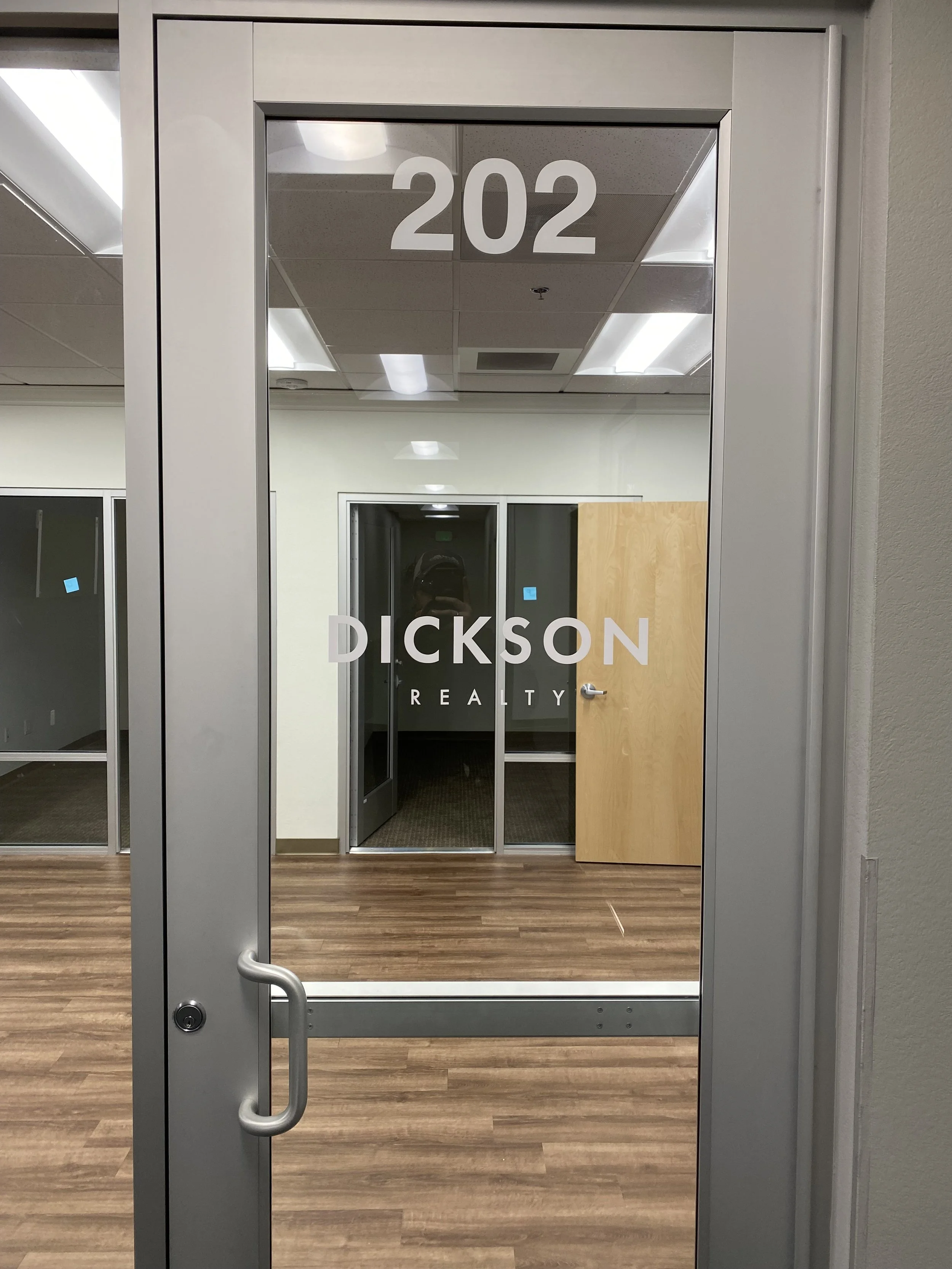 Office door with the number 202 and the logo and name of Dickson Realty, with a wooden door and glass walls inside the office.