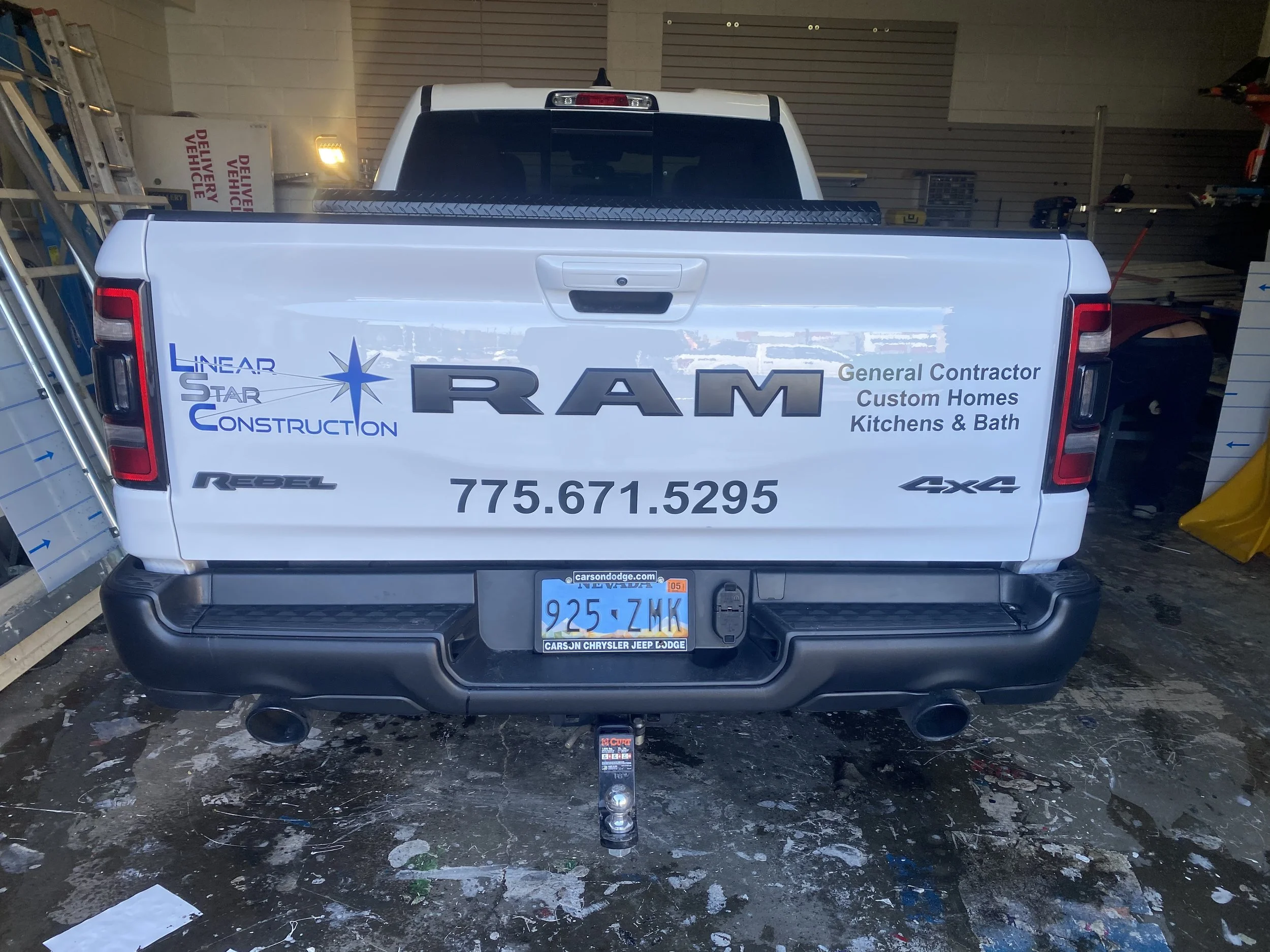 The back of a white RAM pickup truck with a graphic advertisement for Linear Star Construction, a general contractor for custom homes, kitchens, and baths. The advertisement includes a blue star logo, company name, phone number 775.671.5295, and indi