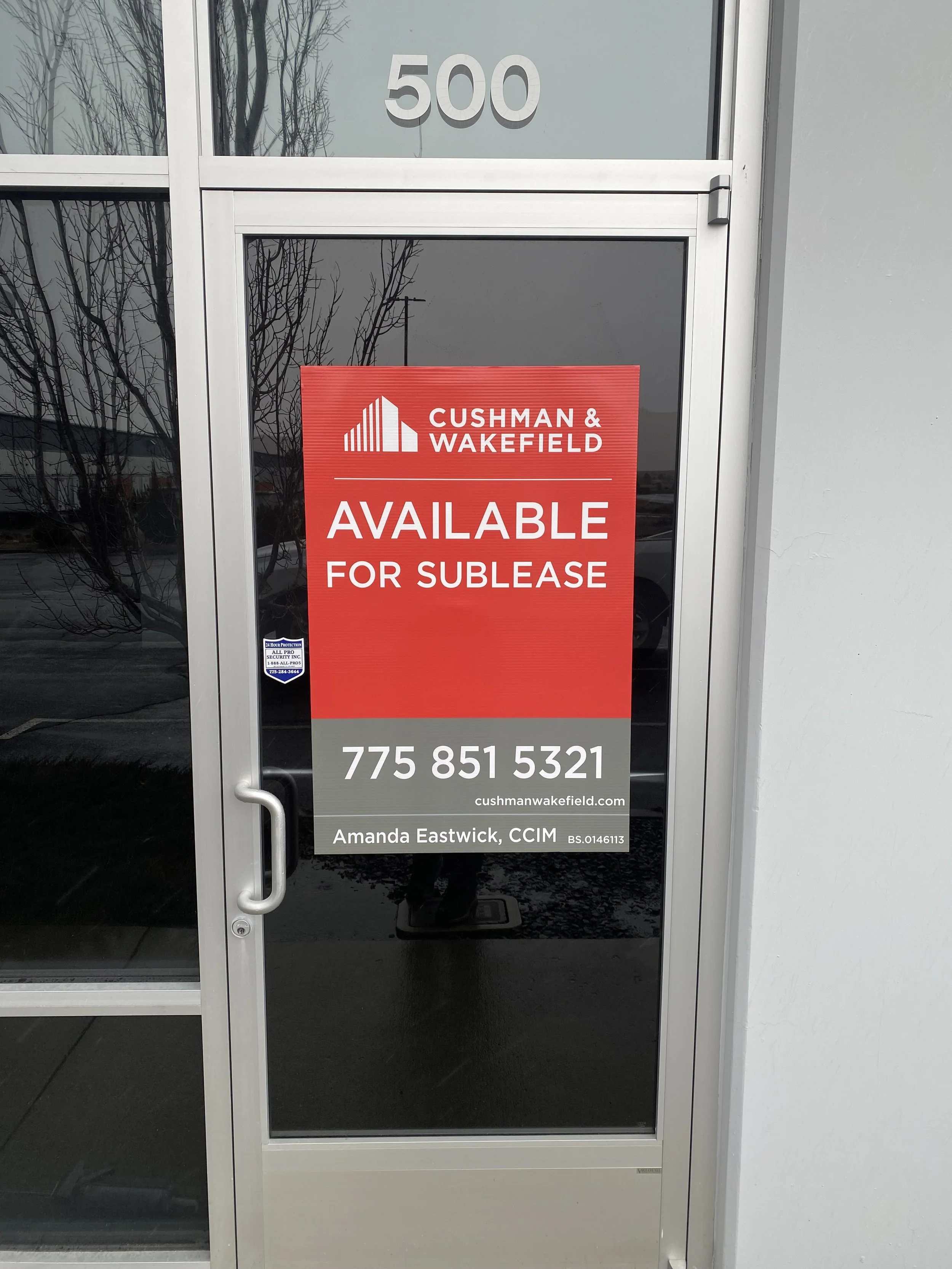 Glass door with a red sign advertising available lease space from Cushman & Wakefield, including contact details and broker information.