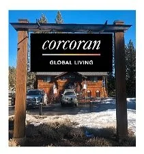 Corcoran sign with 'Global Living' underneath, set in a wooden frame in an outdoor parking area with cars and trees