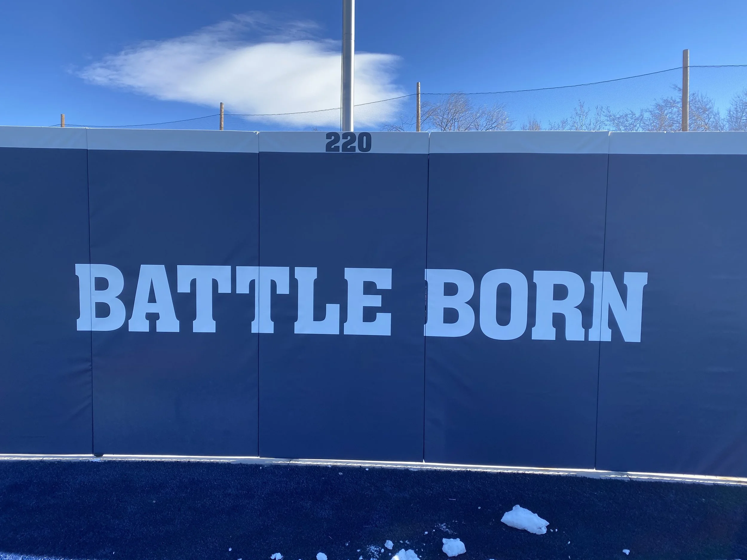 A large blue wall with the words "BATTLE BORN" written in bold white letters. The wall has a number 220 at the top, with a mostly clear sky and some trees in the background.