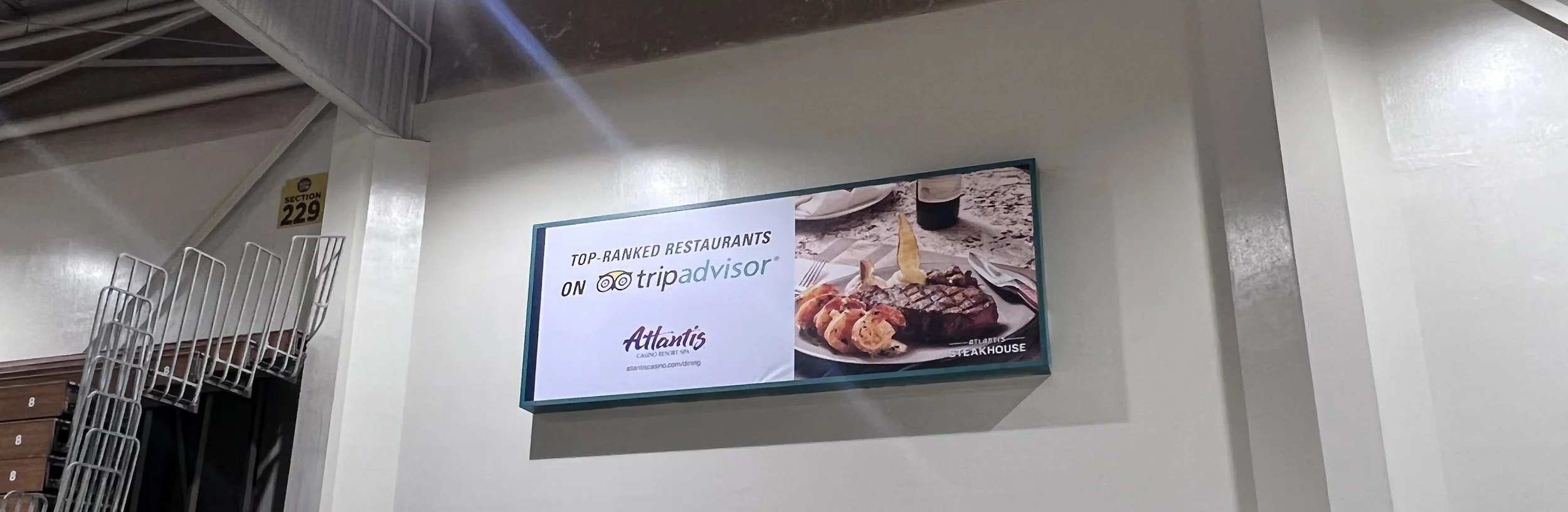 Digital sign advertising Atlantis Casino Resort Spa as a top-ranked restaurant on TripAdvisor, featuring an image of a steak with grilled vegetables on a beach.