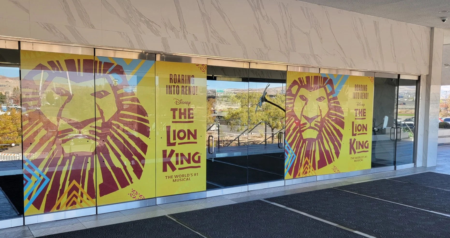 The Grand Sierra Resort has large bright posters displaying a graphic of a lion's face and text promoting Disney's The Lion King musical, with the phrases "Roaring into Reno!" and "The World's #1 Musical".