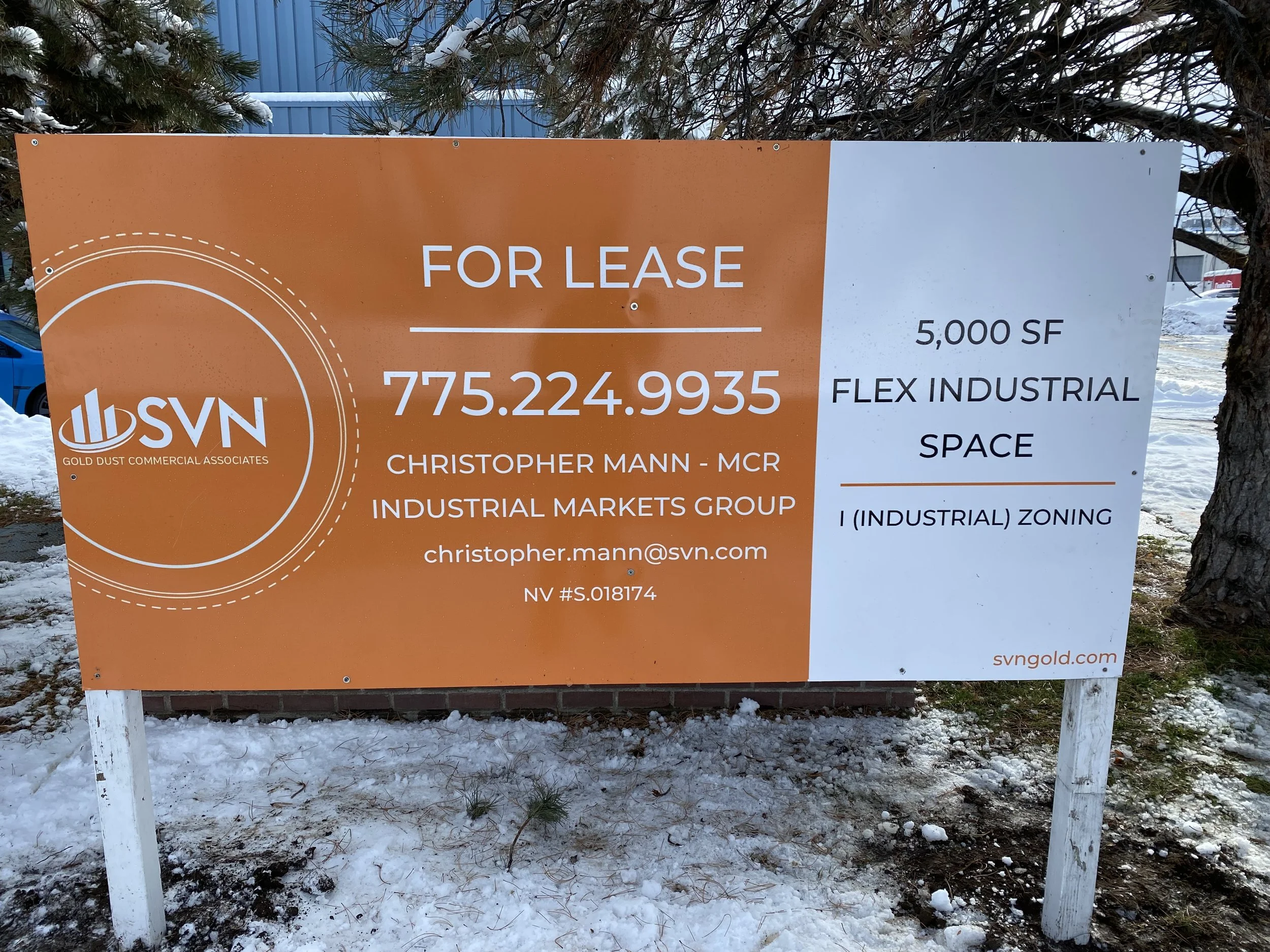 Sign advertising industrial space for lease, 5,000 square feet, located in an industrial zone, contact information for Christopher Mann, with snow-covered ground and trees in the background.