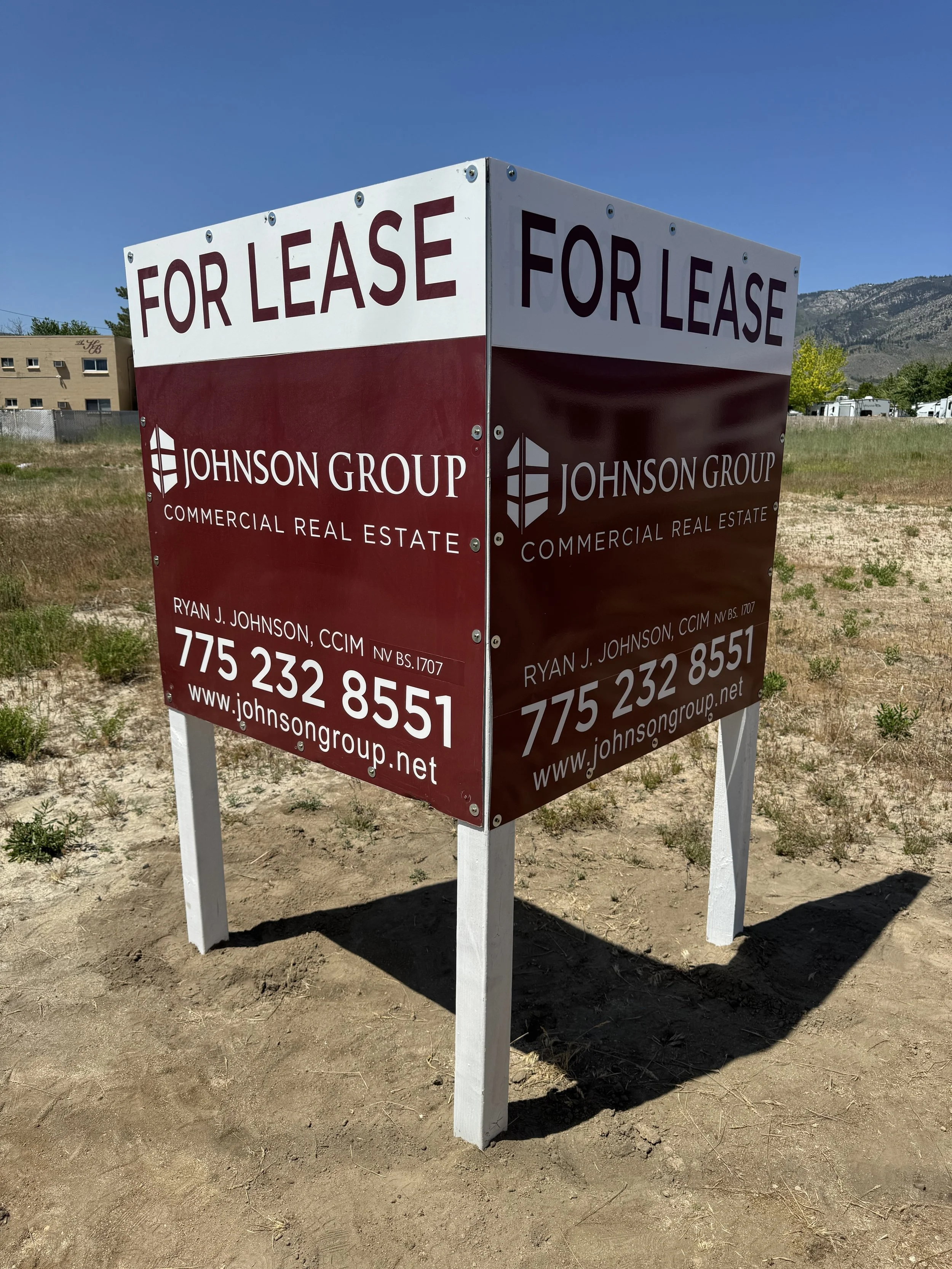 A large outdoor sign with the words 'For Lease' in red letters at the top, advertising commercial real estate by Johnson Group. The sign includes contact information for Ryan J. Johnson, CCIM, and a website address.