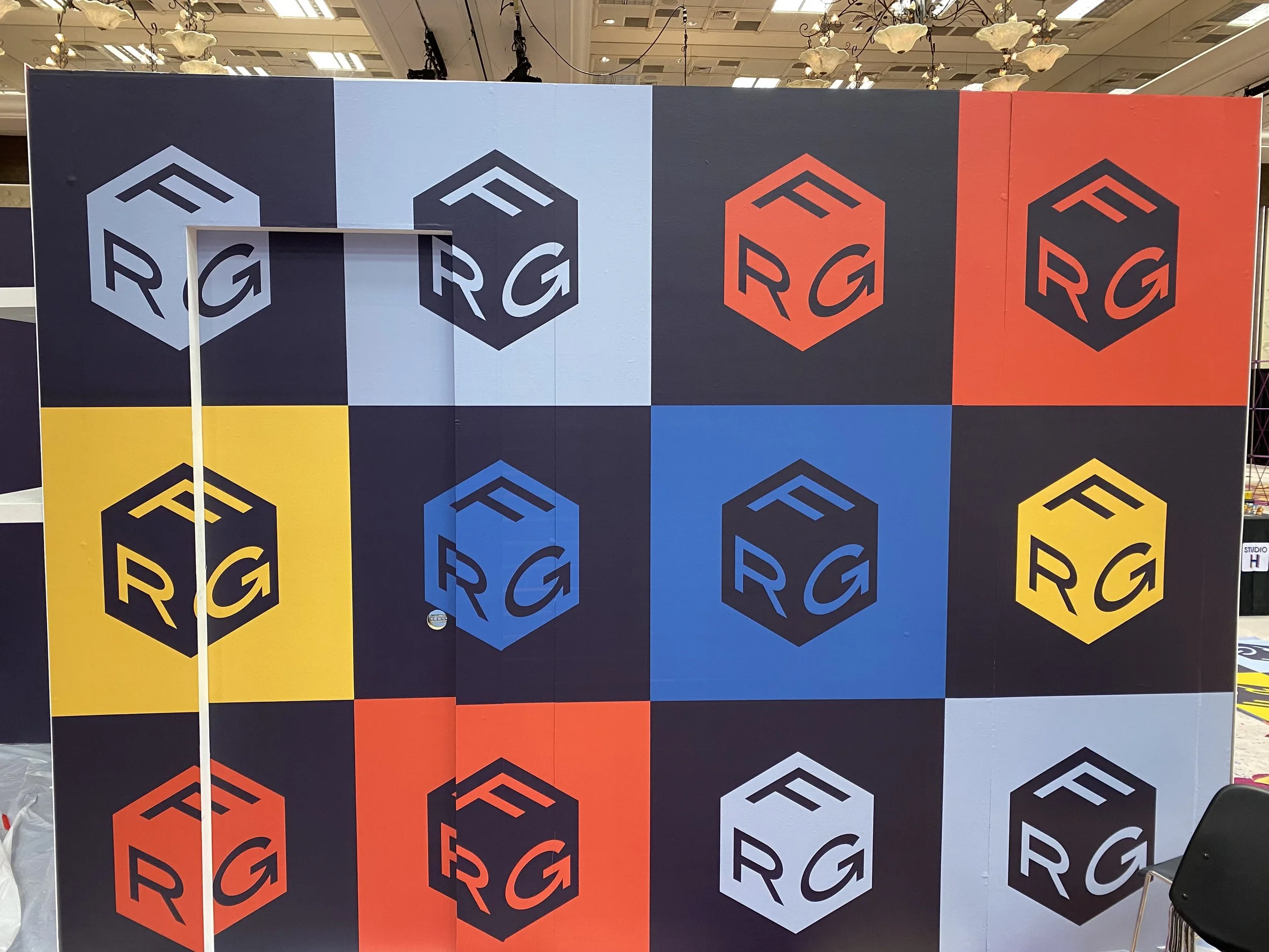 A colorful display wall with repeating patterns of a black cube logo with the letters 'RG' in various colors including white, black, red, yellow, and blue, set against a background of colorful solid blocks.