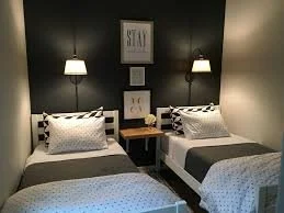 Two twin beds with black and white bedding, nightstands, and wall-mounted lamps in a bedroom with dark green and beige walls.