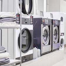 Laundry area with three washing machines and a shelf of folded towels.