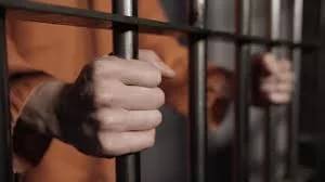 Person gripping prison bars in a jail cell.