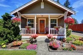 Front view of a cozy house with a small porch, surrounded by colorful flowers and greenery.