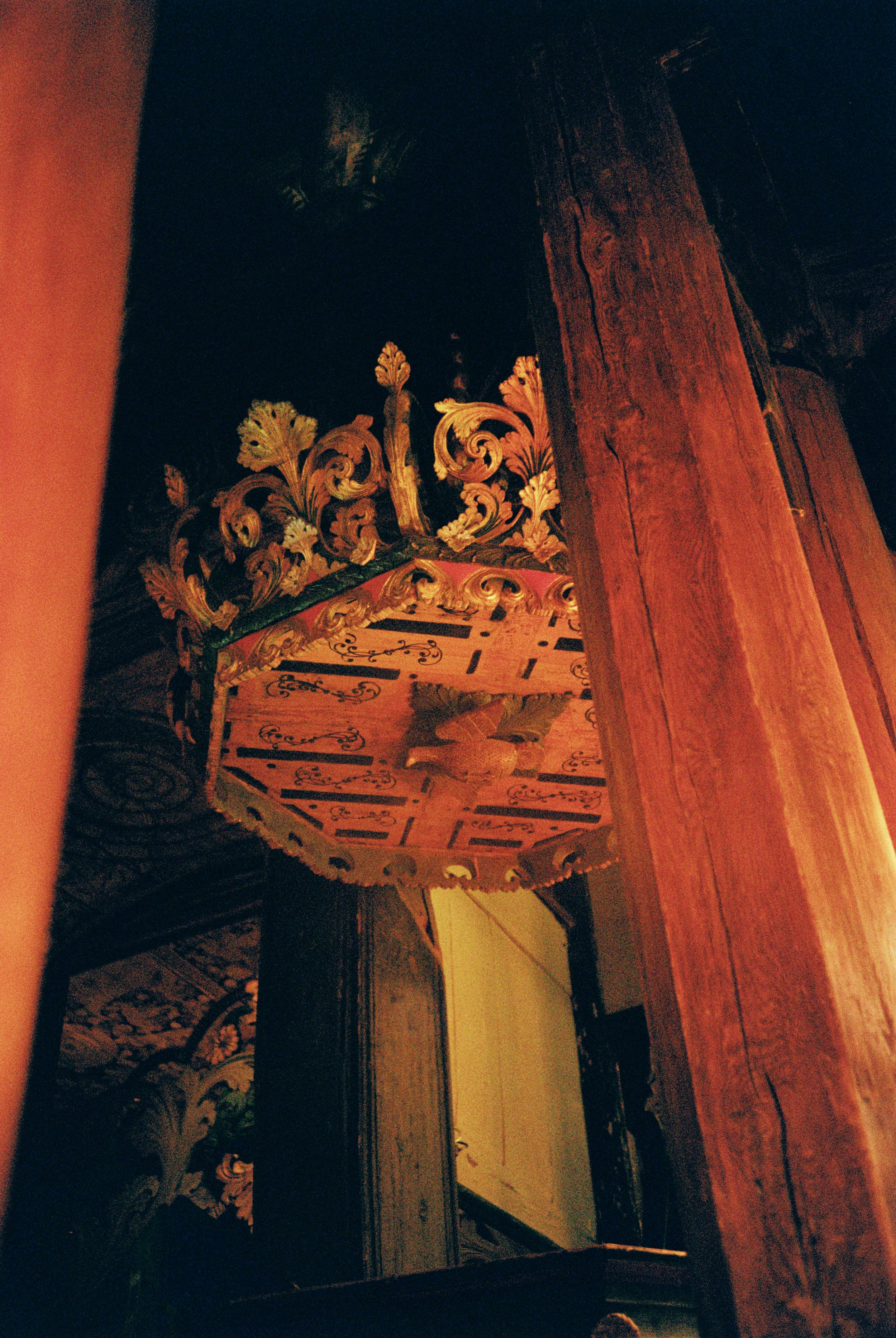Ornate wooden chandelier with floral and leaf designs hanging from a wooden ceiling in a dimly lit room.