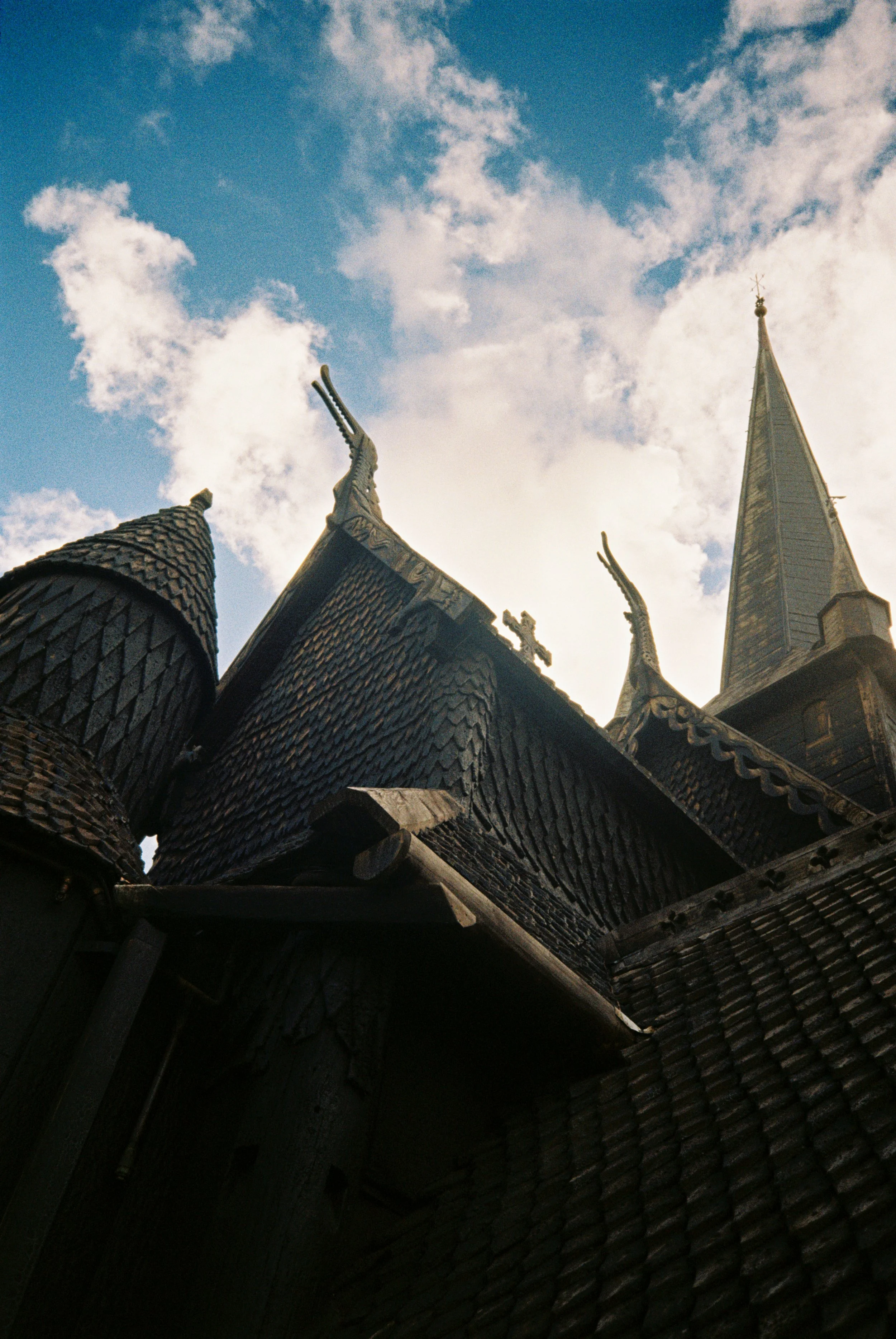 Photo of a historic church with wooden shingle roofing, ornate steeples, and tower against a partly cloudy sky.