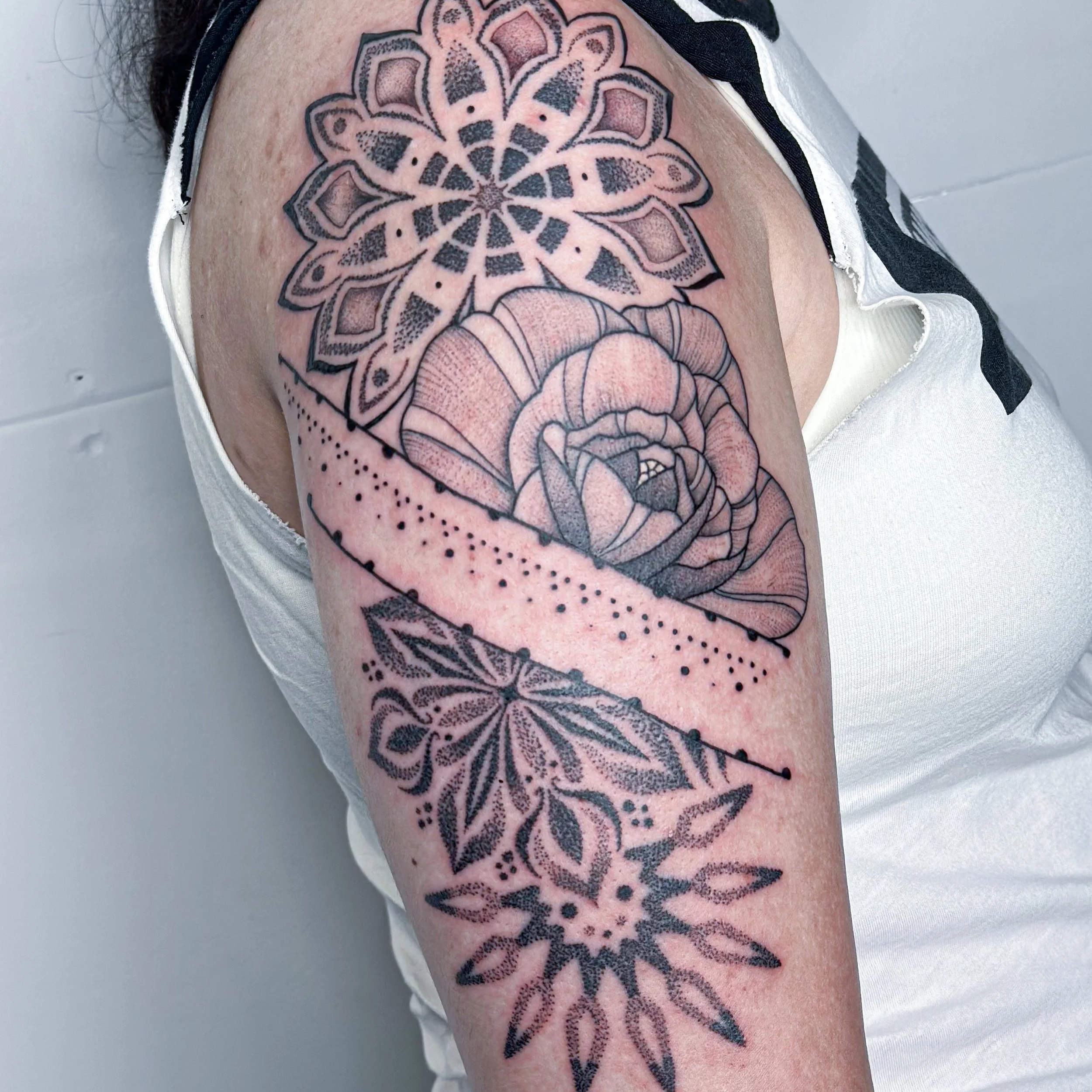 Tattoo of a mandala, a rose, and a sunburst on a person's upper arm.