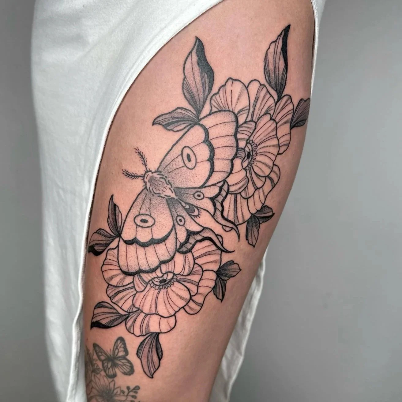 Black outline tattoo of butterflies and flowers on a person's upper arm.