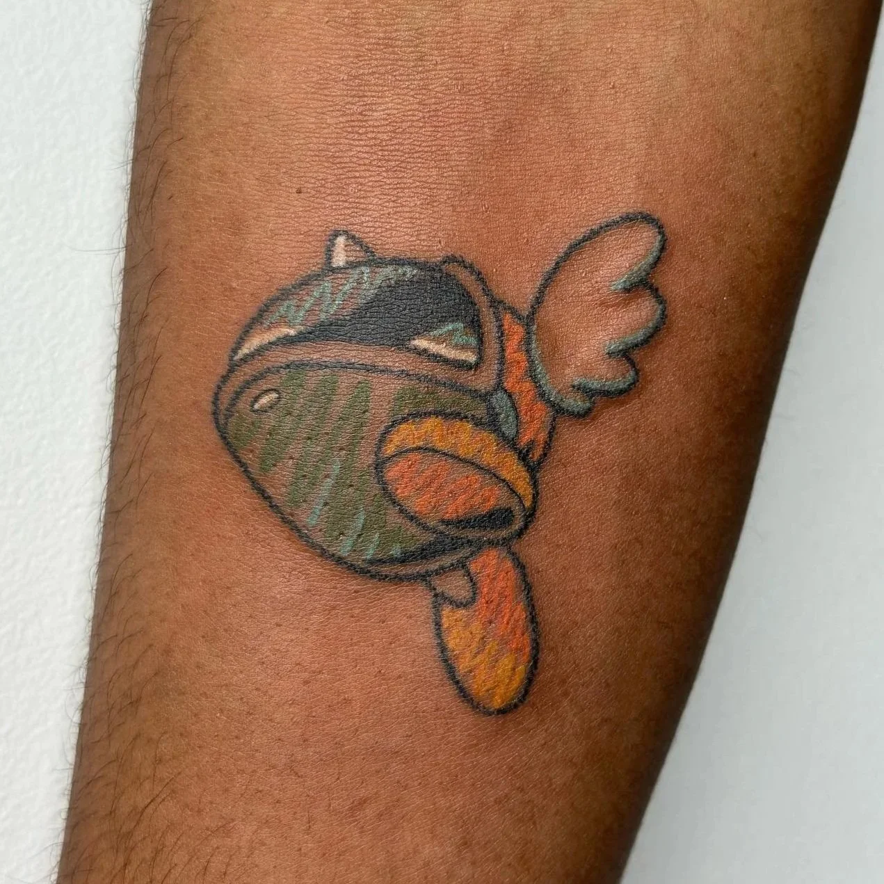 Colorful tattoo of a bee with wings, fruit pattern on the head, and a slightly open mouth on a person's arm.