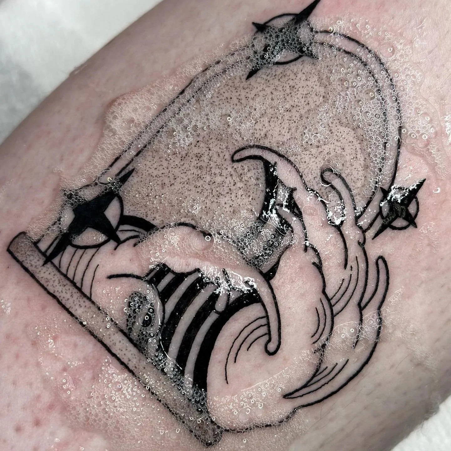 Tattoo of a skull, an hourglass, a star, and other symbols on skin, surrounded by soap bubbles.