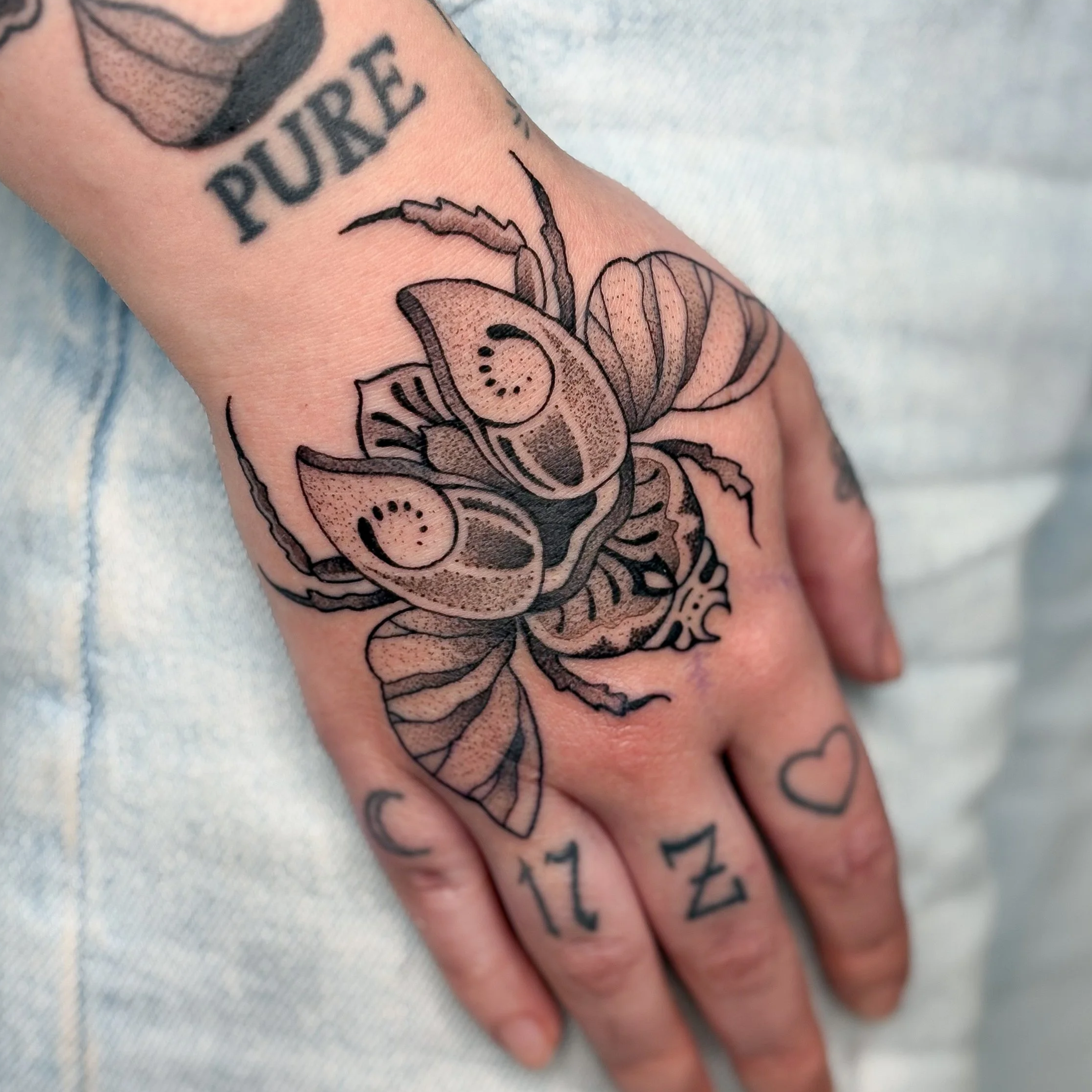 Black line tattoo of a bee on a person's hand, with the words 'PURE' on the wrist and the numbers '17' and '21' with a heart symbol tattooed on the fingers.
