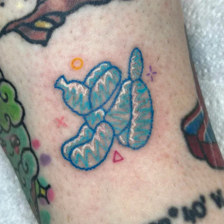 Tattoo of a butterfly with blue outlines, zigzag wing patterns, surrounded by small colorful shapes and symbols, on skin.