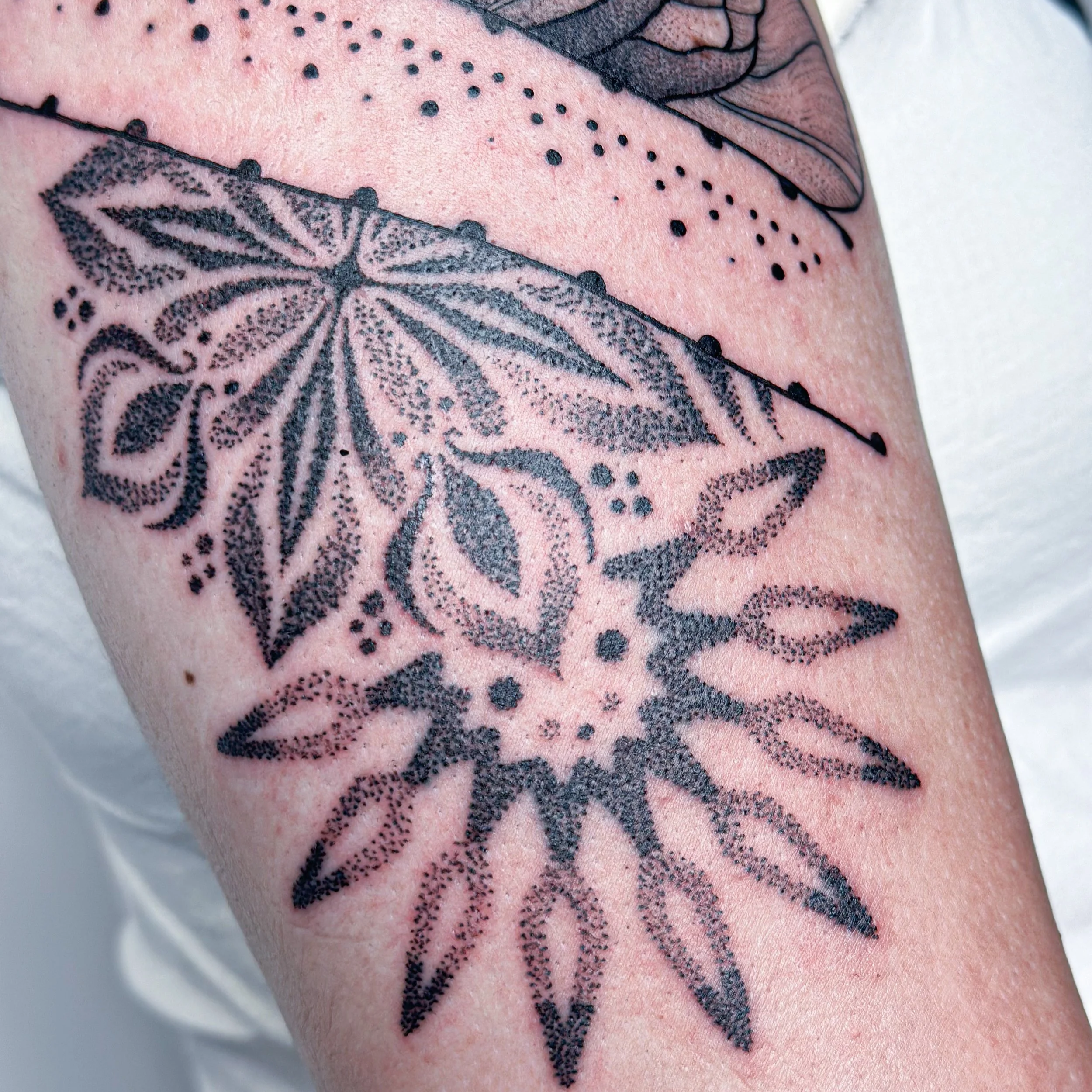 A black dotwork tattoo of a detailed floral and leaf design on skin.