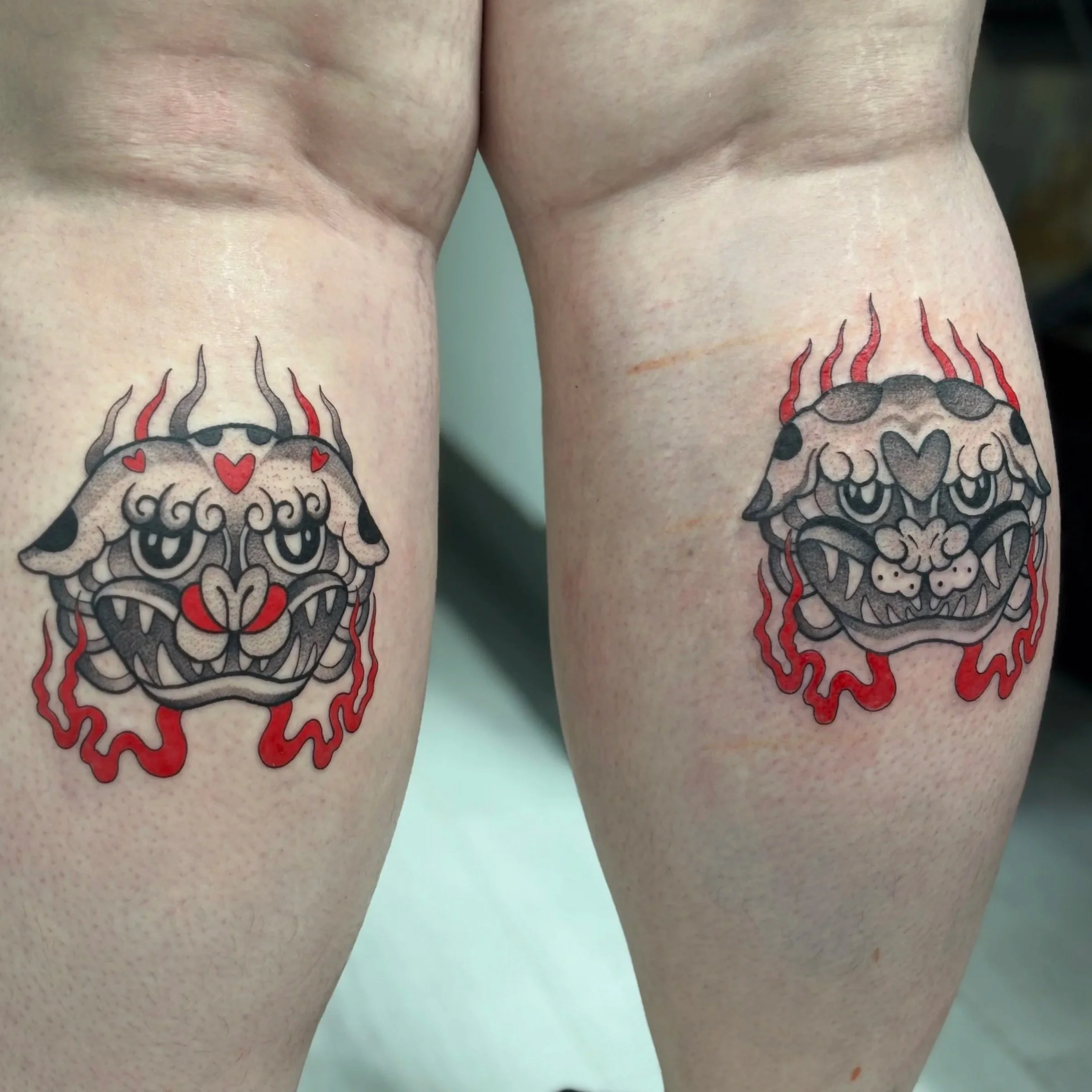 Pair of colorful dragon head tattoos on upper thighs featuring black, red, and gray ink with heart and flame details.