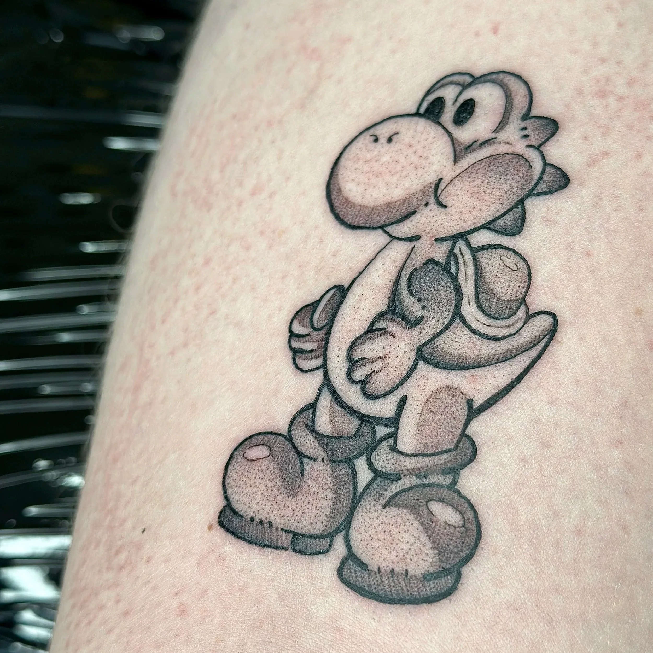 Tattoo of Yoshi, a character from Super Mario, in black ink with shading on arm.