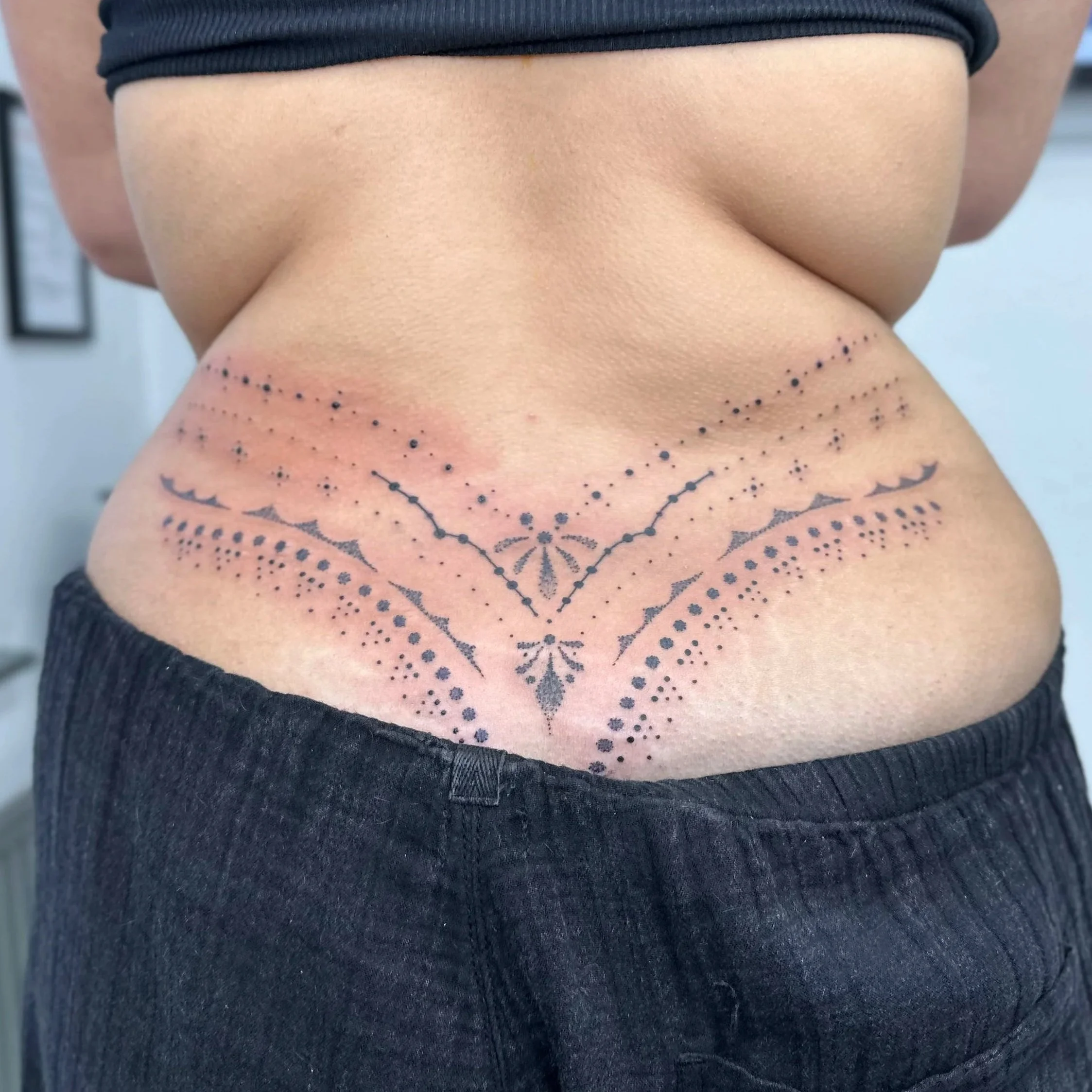 Tattoo with black dot and line patterns on a person's lower back.