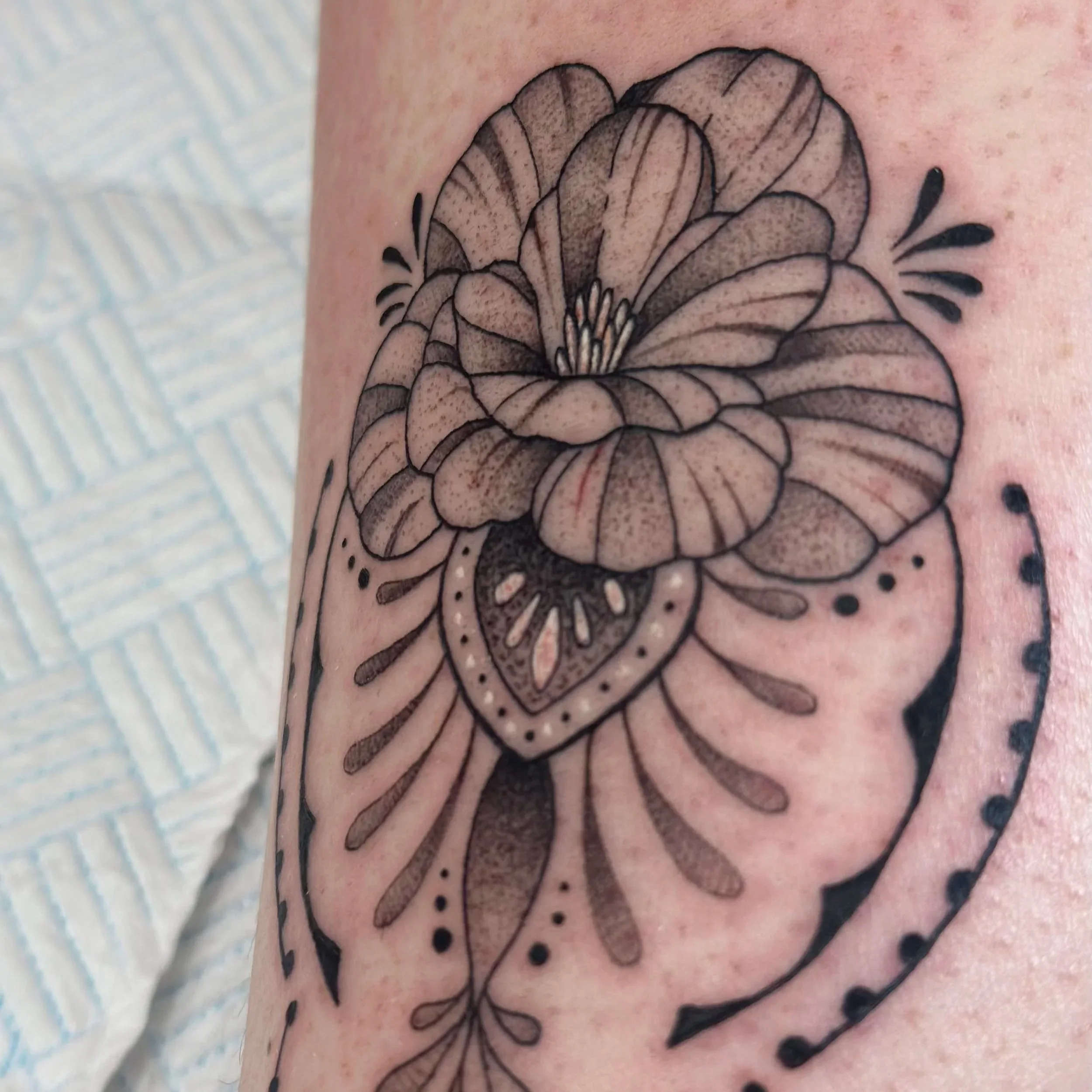 Black and gray floral tattoo featuring a large flower with intricate shading and detailing, accompanied by abstract decorative elements.